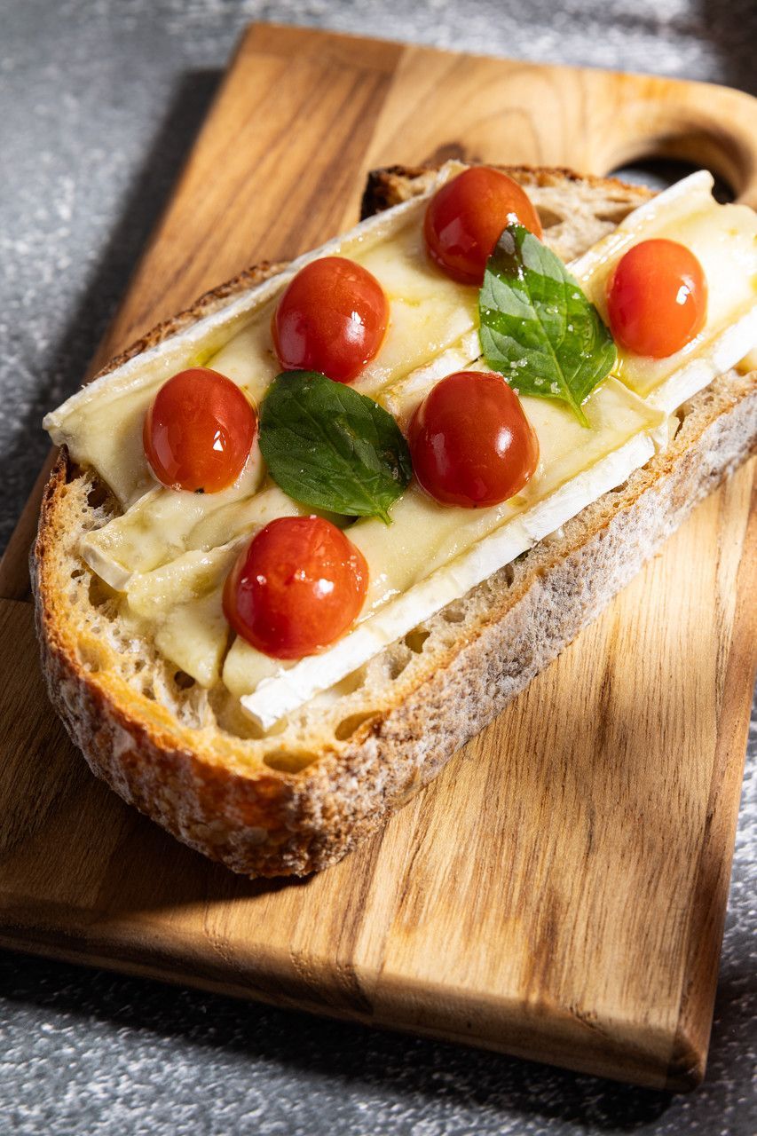 Sanduíche aberto de tomate e manjericão em tábua de madeira.