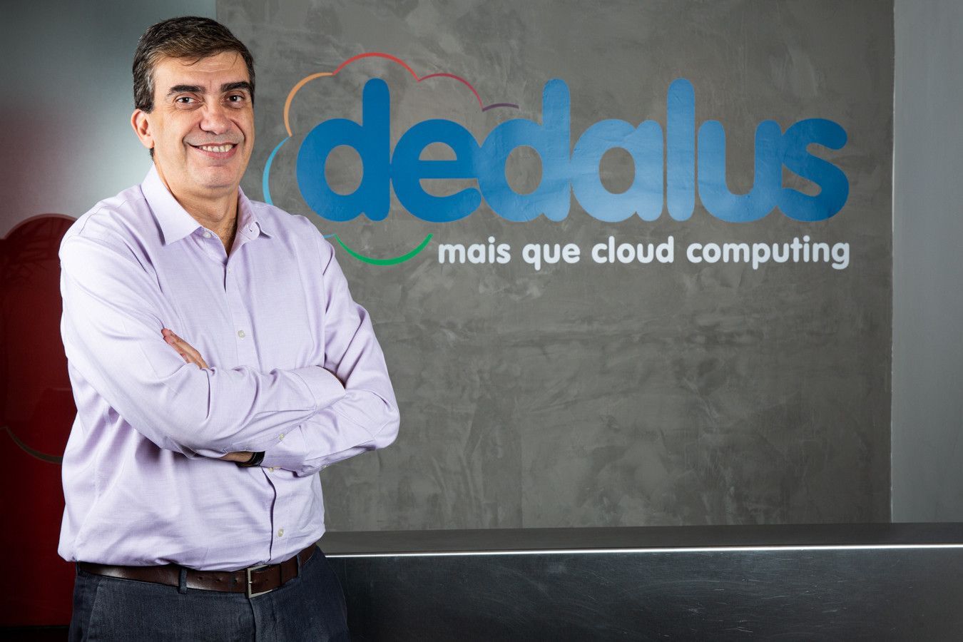 Homem com camisa lilás claro ao lado do logotipo da Dedalus e da placa “mais que cloud computing”