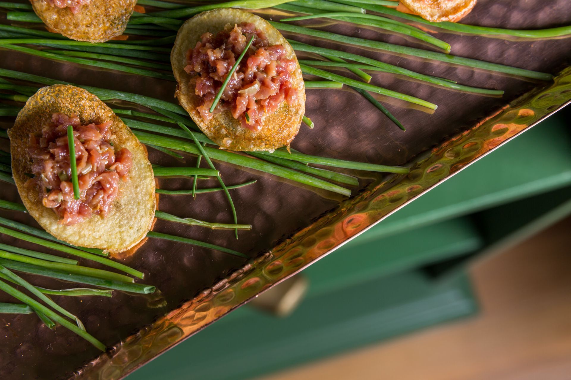 Aperitivos empratados com cobertura rosa em uma bandeja forrada com folhas verdes.