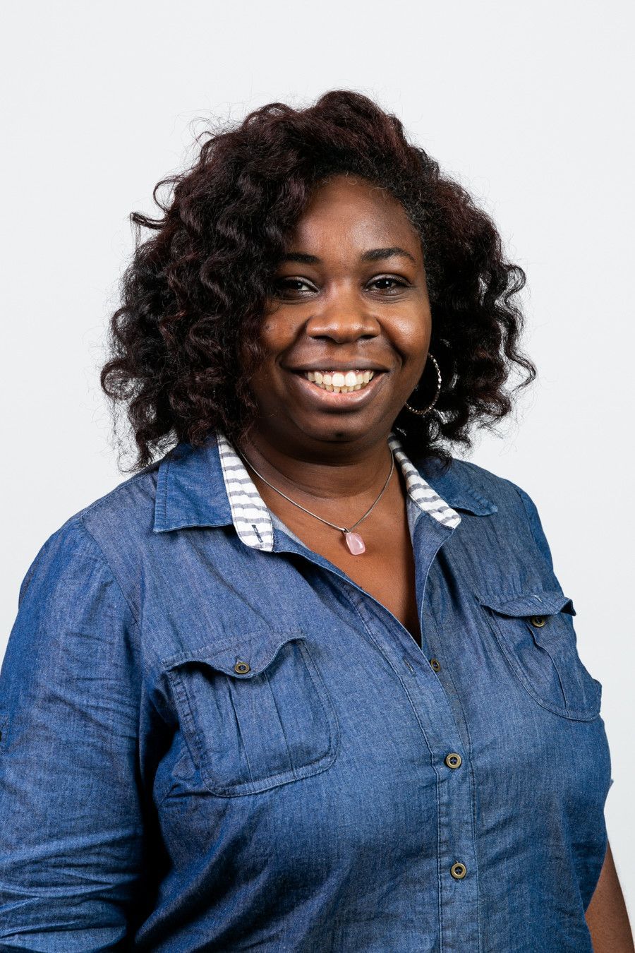 Mulher sorridente com camisa jeans azul contra um fundo claro.