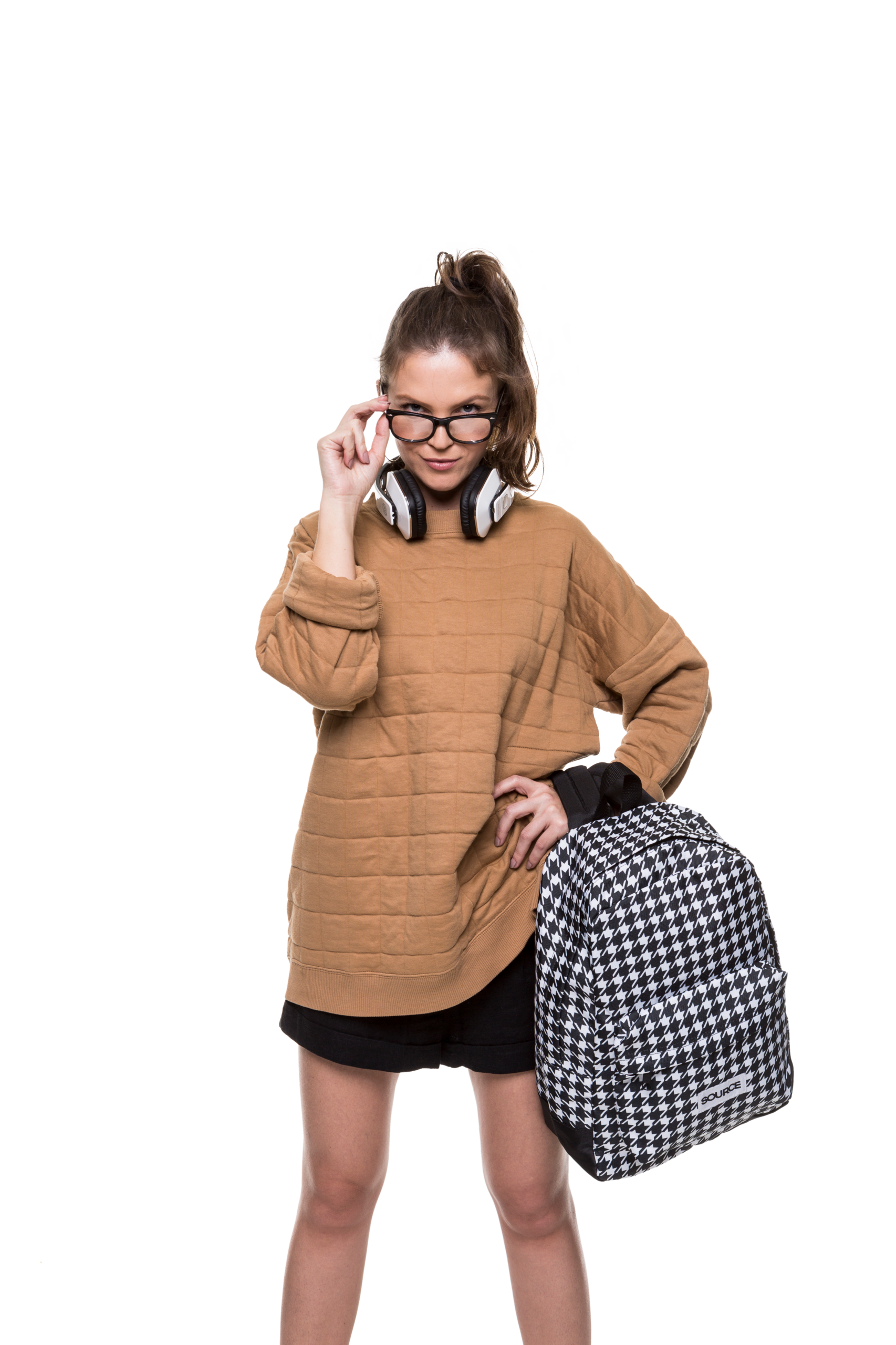 Mulher vestindo um suéter bege, segurando uma bolsa de viagem preta e branca e ajustando os óculos.