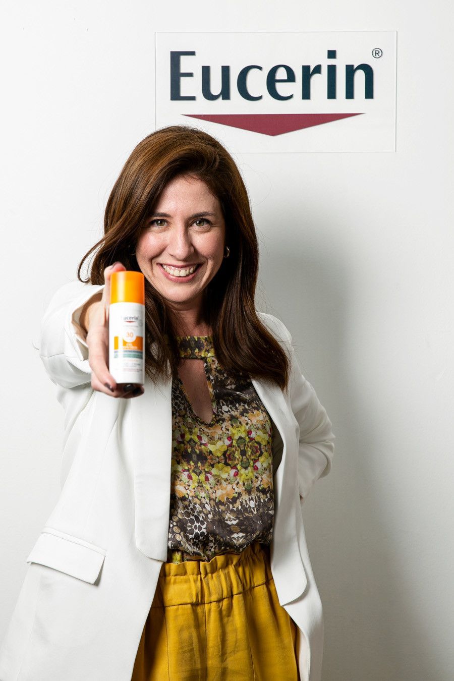 Mulher segurando um produto Eucerin, sorrindo ao lado do logotipo da marca.