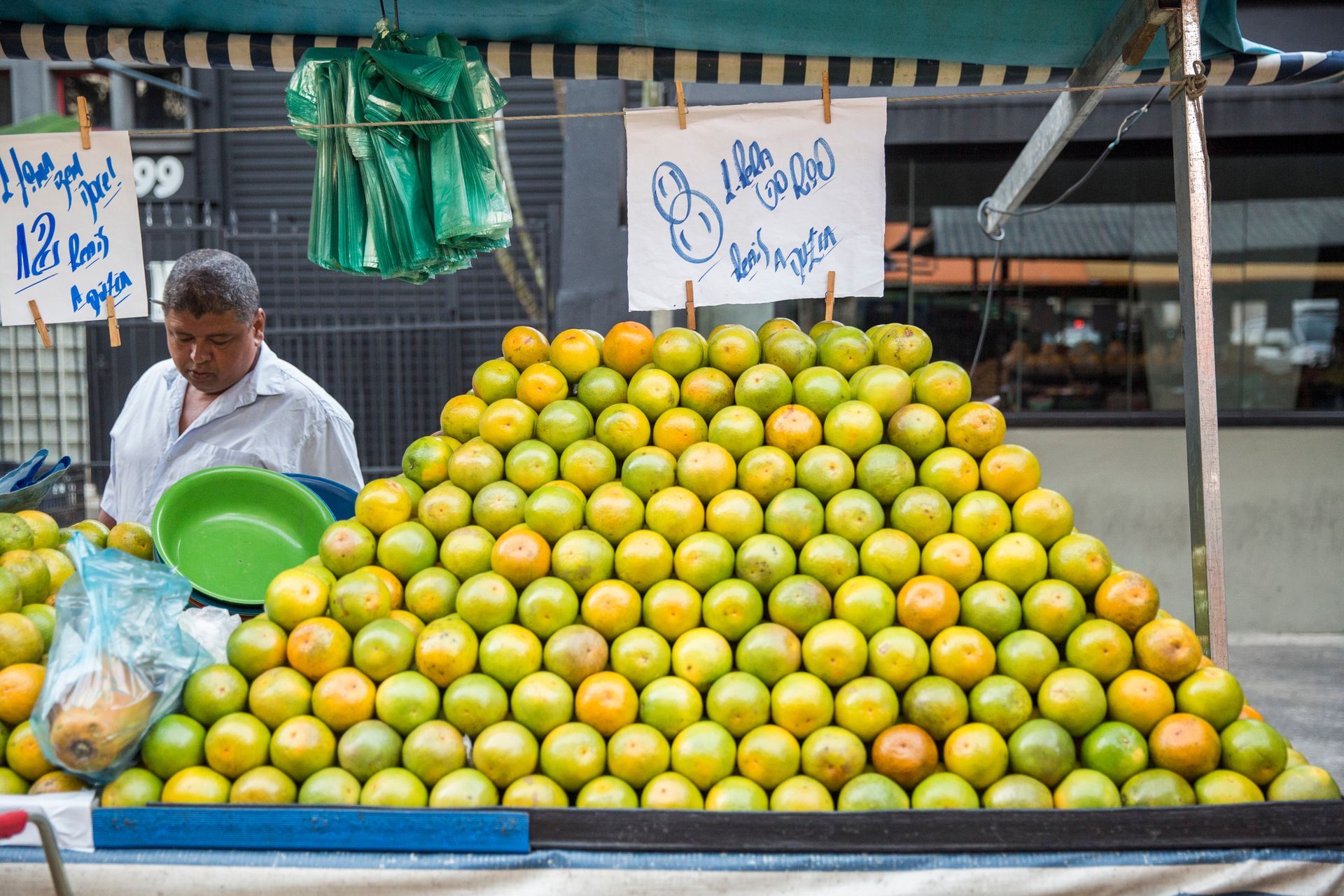 Banca de mercado de rua repleta de frutas verde-amareladas, com um vendedor segurando uma tigela verde.