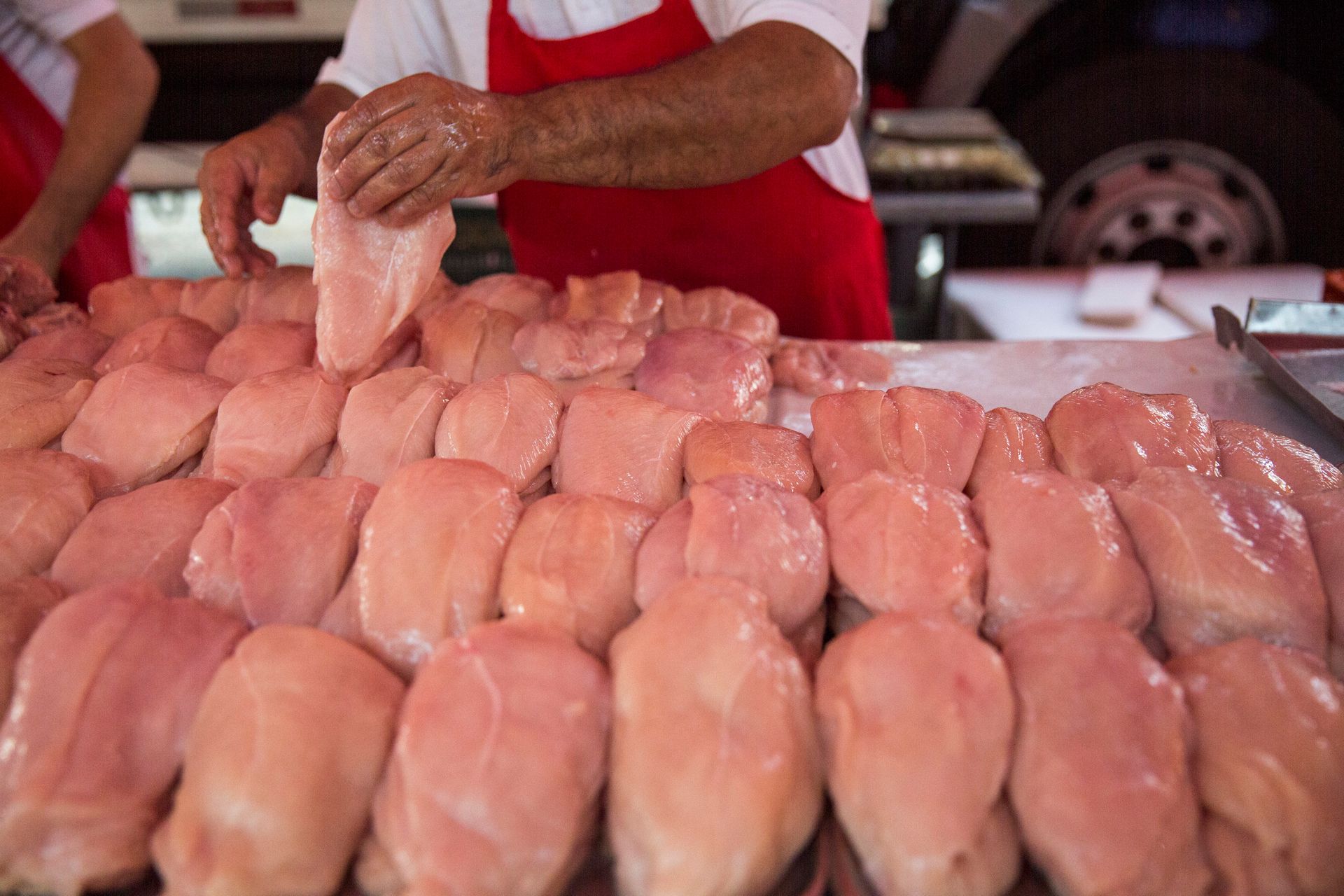Vendedor arrumando peitos de frango crus em uma barraca de mercado.