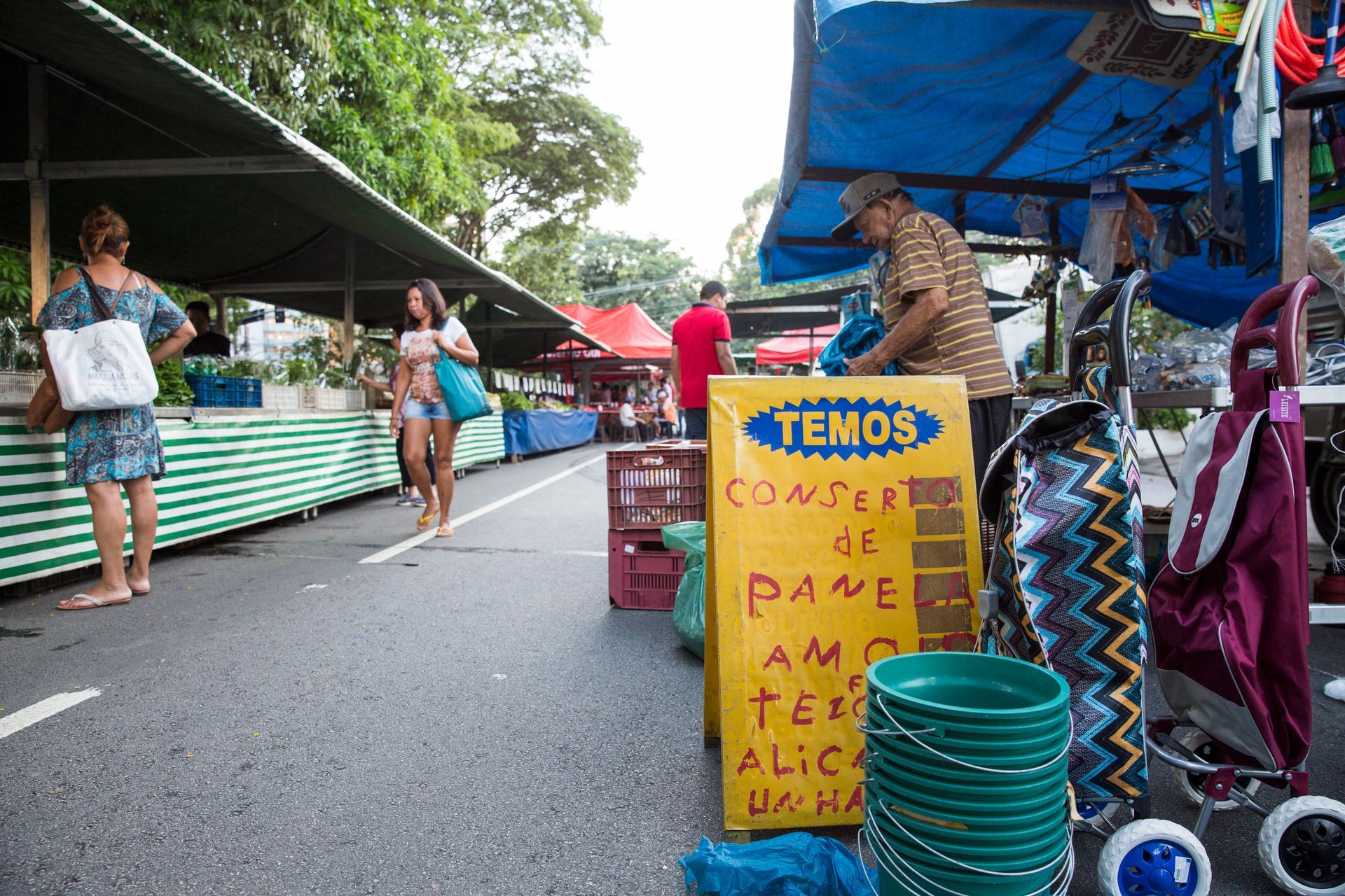 Barraca de mercado ao ar livre com tigelas de plástico turquesa e uma placa amarela com a inscrição “TEMOS” sob uma lona azul.