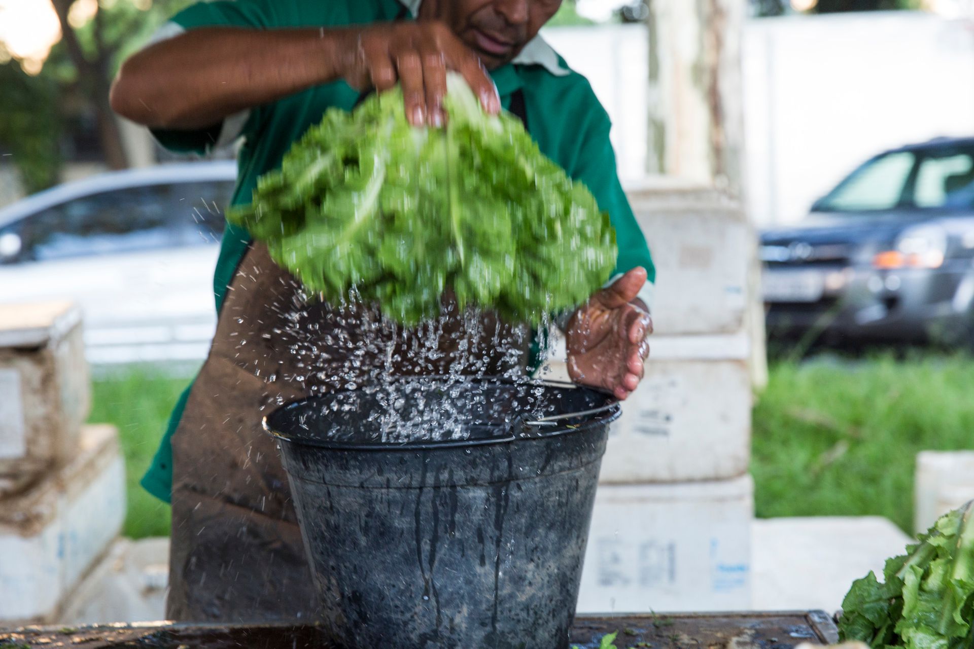 Pessoa lavando verduras em um balde preto ao ar livre