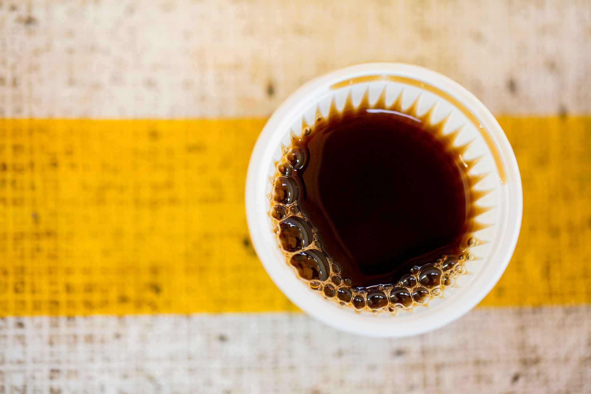 Xícara de café preto sobre uma mesa rústica com uma faixa amarela.