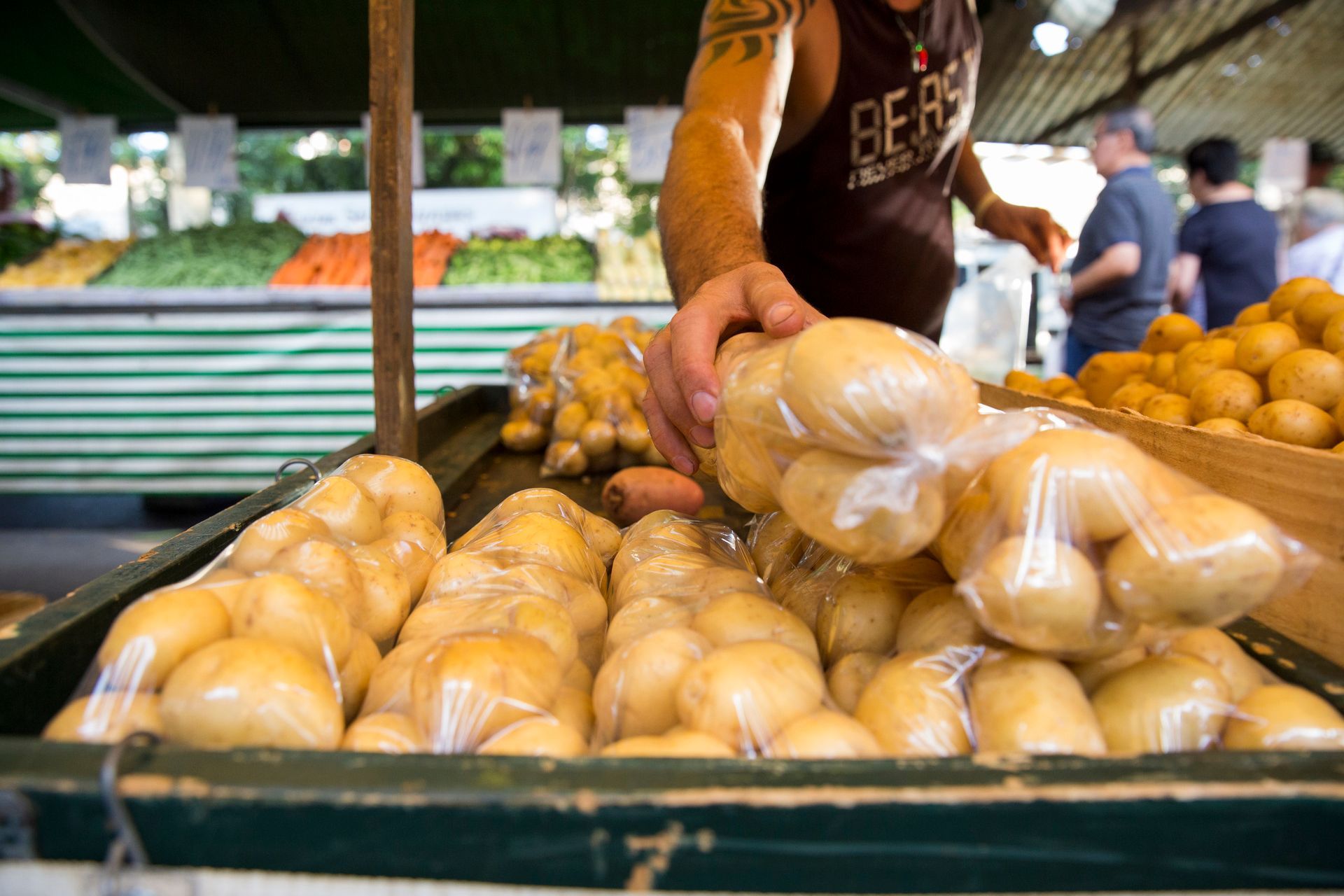 Vendedor entregando pãezinhos embalados em uma barraca de mercado ao ar livre.
