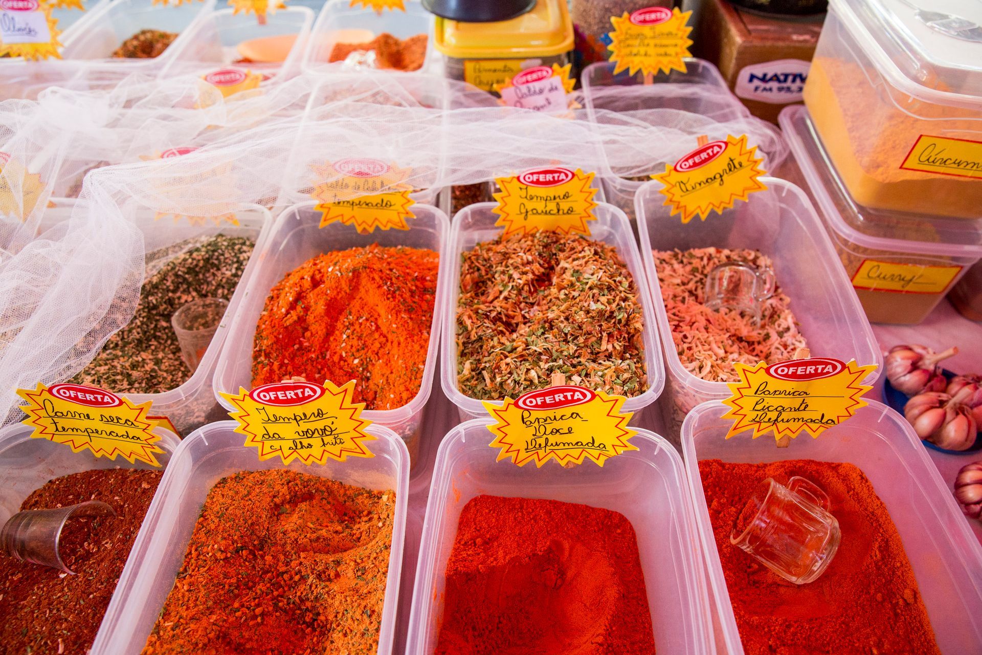Variedade de especiarias e temperos coloridos em recipientes de plástico transparente em uma barraca de mercado.