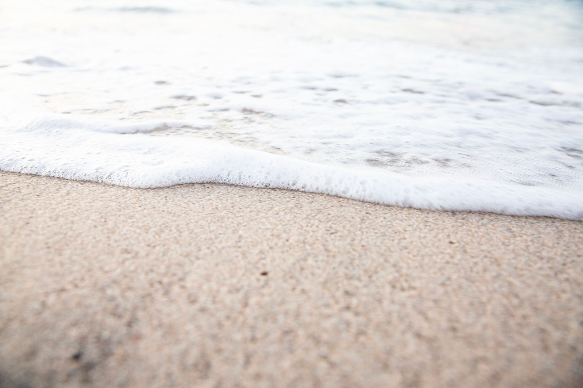 Ondas brancas e espumosas quebrando em uma praia de areia bege