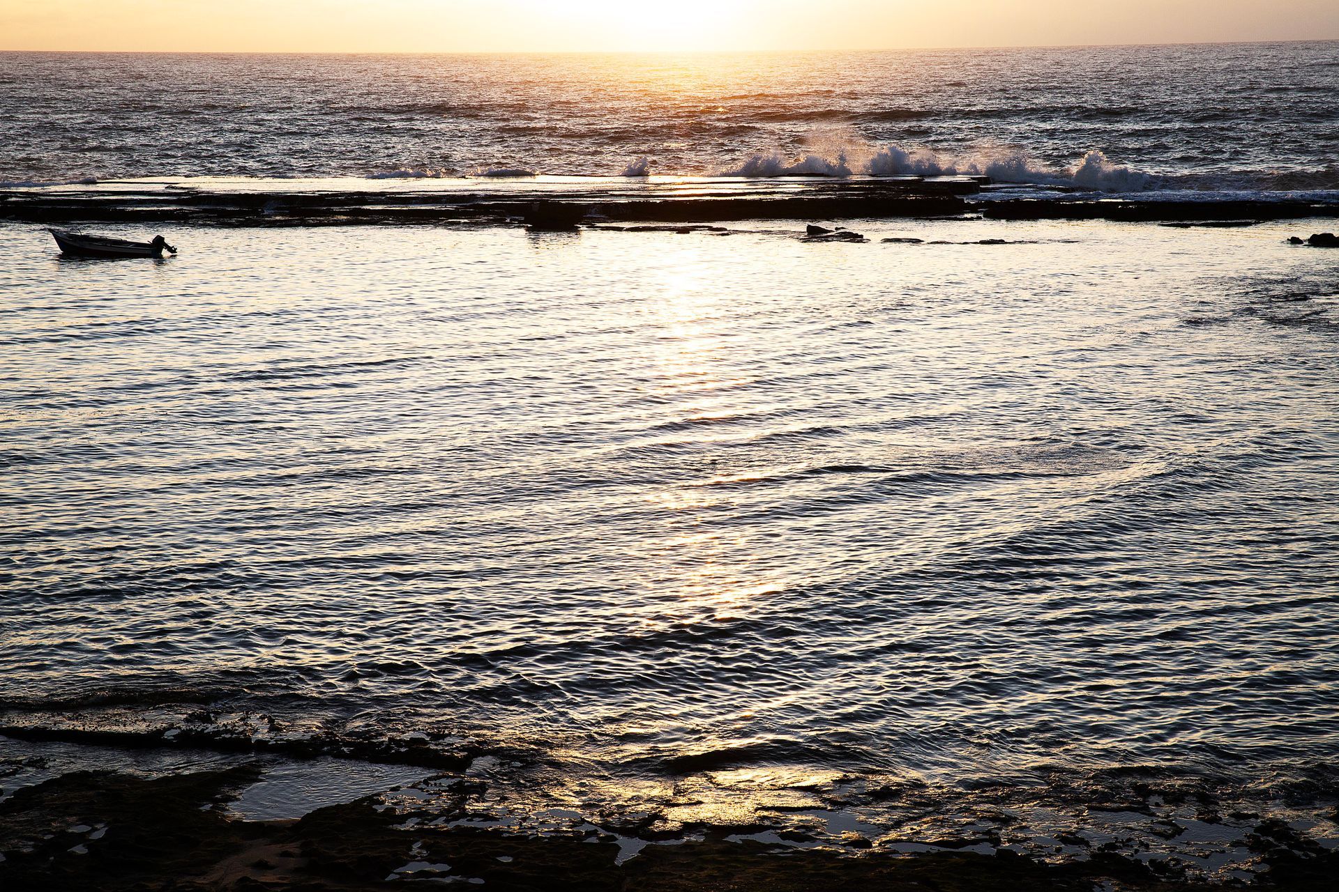 Ondas do oceano iluminadas pelo sol cintilando ao pôr do sol sobre uma costa rochosa.