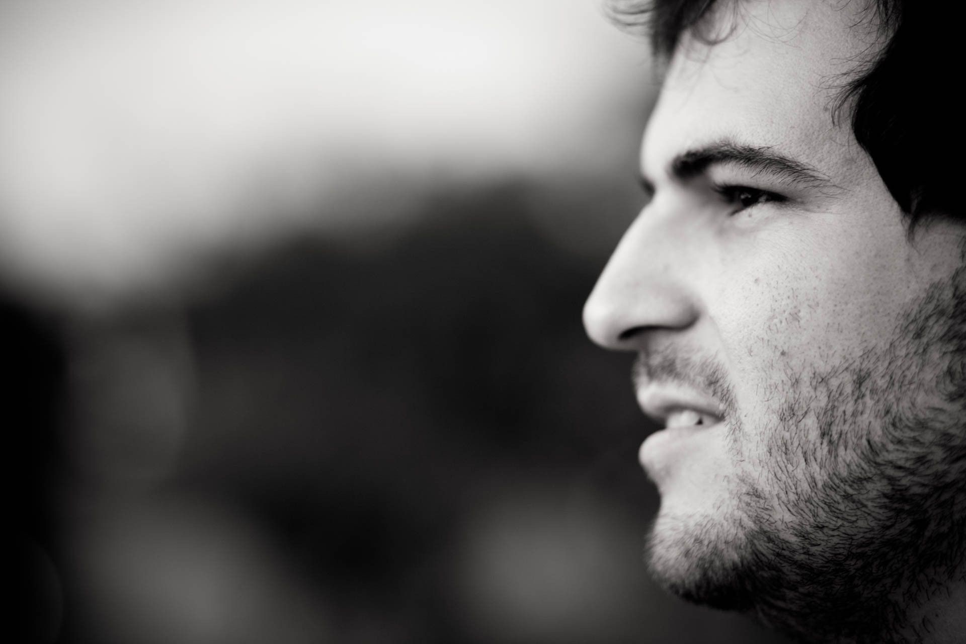 Perfil em preto e branco de um homem sorridente contra um fundo desfocado.