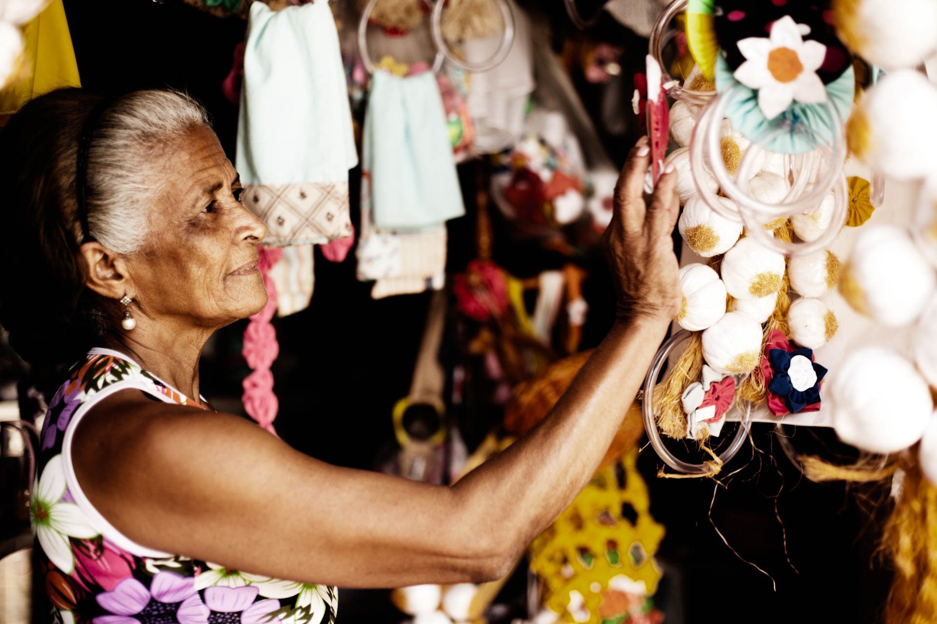 Mulher arrumando decorações de conchas e flores penduradas em uma barraca de mercado.