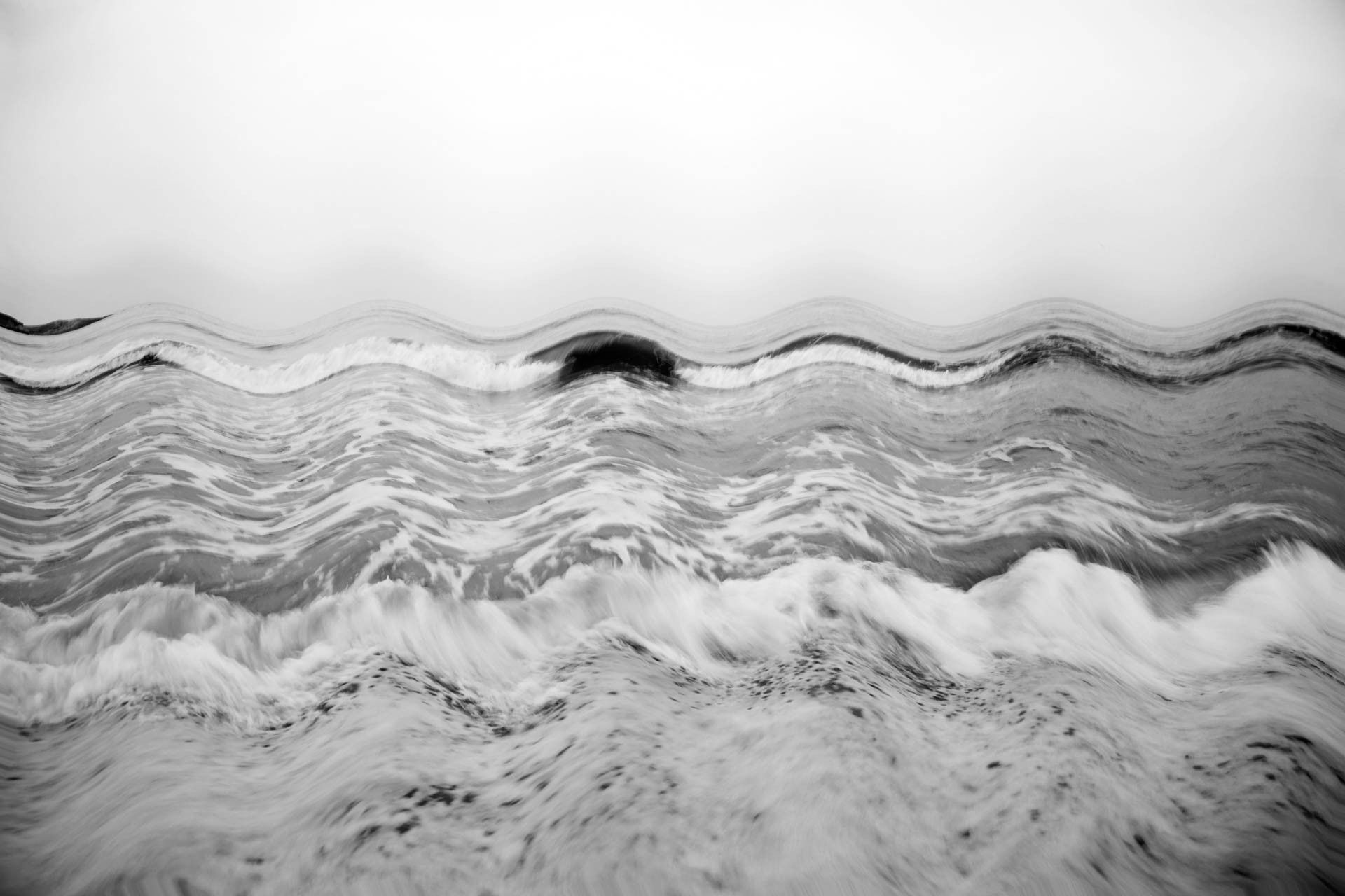 Superfície oceânica ondulada em preto e branco com espuma ondulante e horizonte nebuloso.