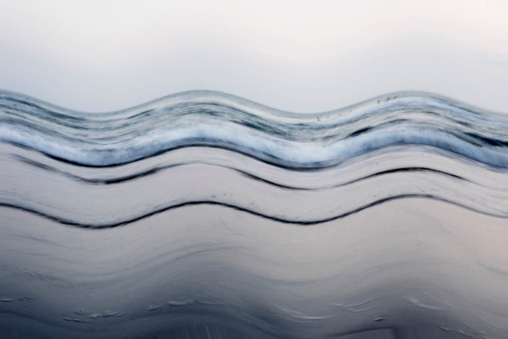Ondulações abstratas em tons de azul acinzentado, semelhantes a ondas, em uma superfície de água lisa.