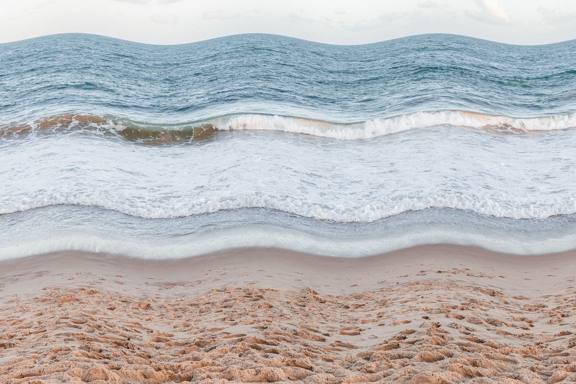 Ondas azuis suaves banhando uma praia de areia sob um céu pálido.