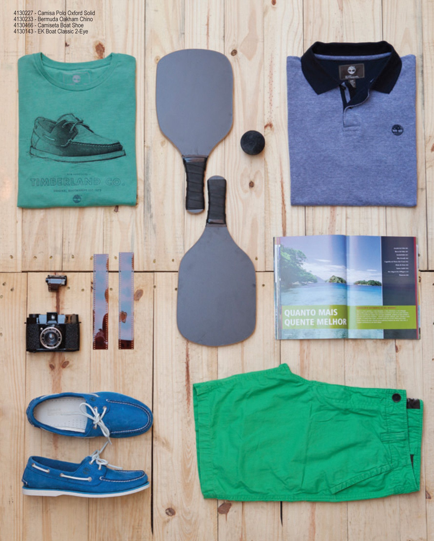 Diversas roupas e equipamentos dispostos em um piso de madeira, incluindo camisas, remos, sapatos e uma câmera.