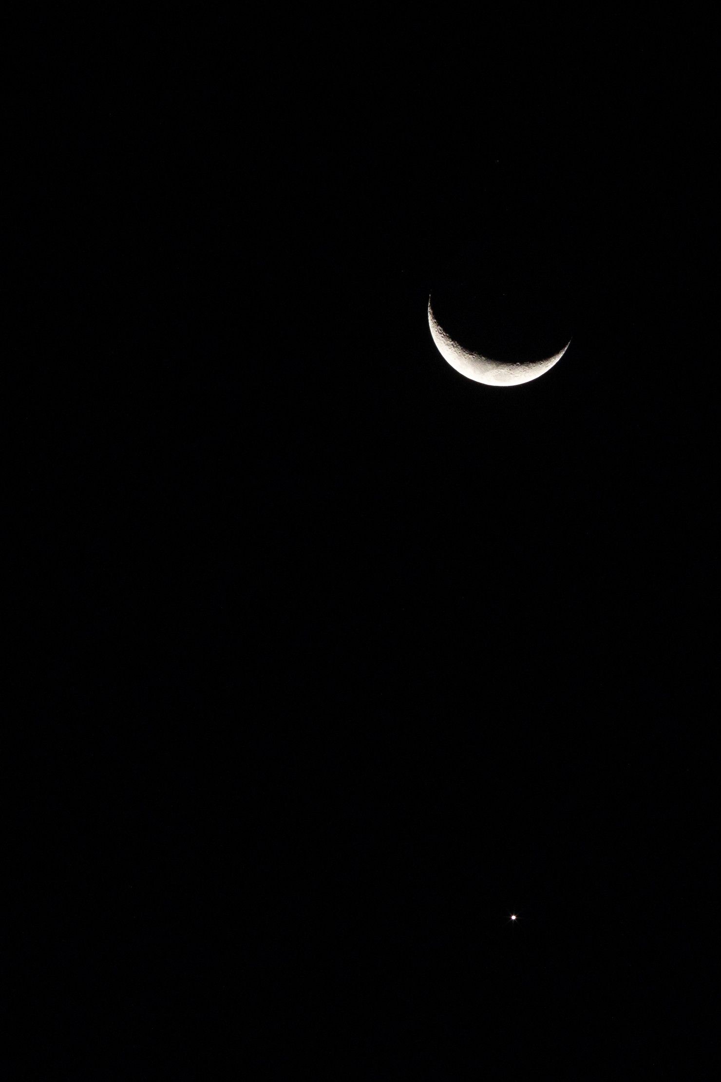 Uma fina lua crescente em um céu noturno escuro com uma pequena estrela brilhante abaixo dela.