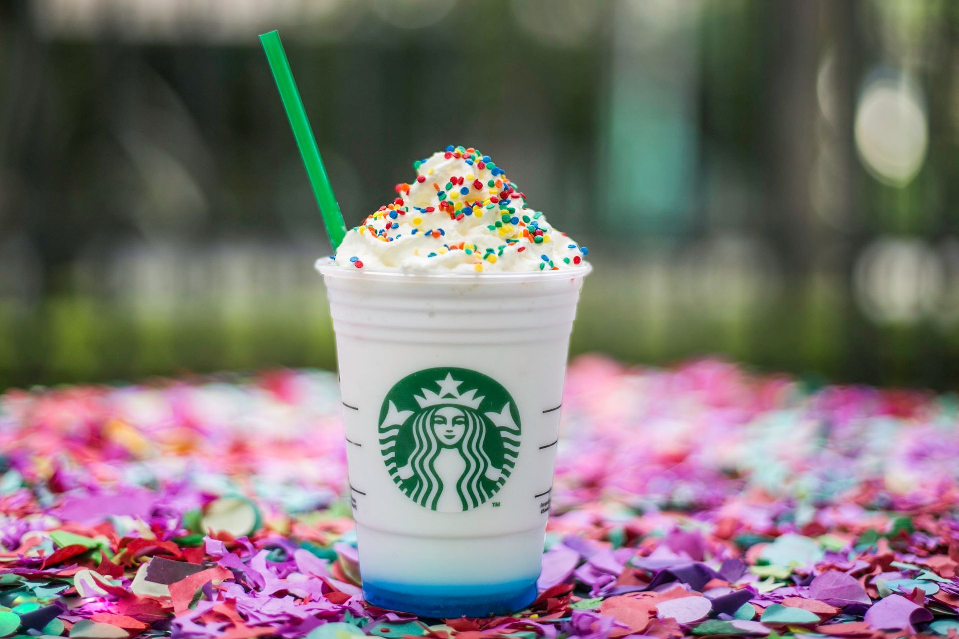 Copo da Starbucks com chantilly e canudo verde sobre uma superfície coberta de confete.