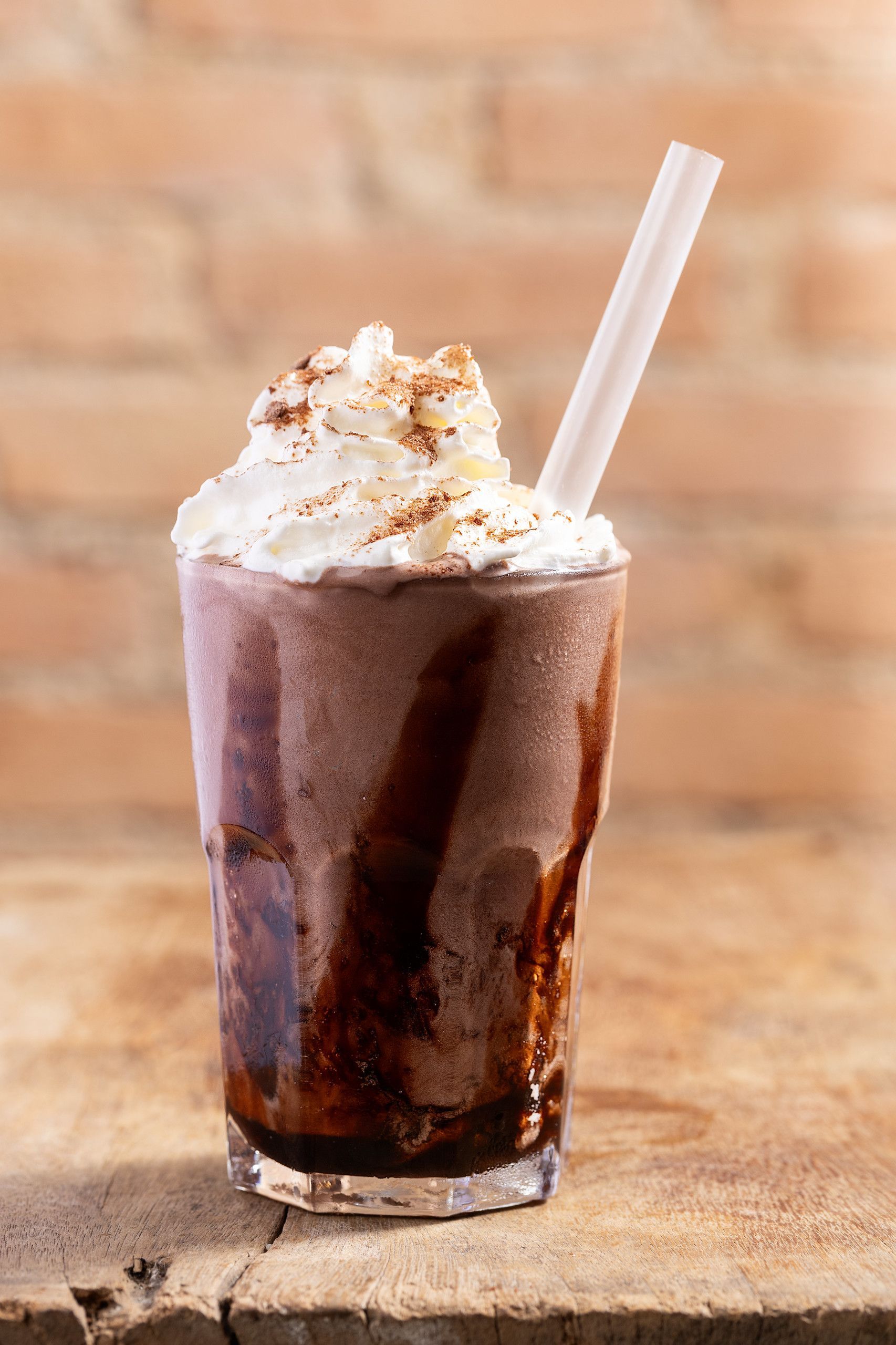 Milkshake de chocolate com chantilly e canudo sobre uma mesa de madeira.