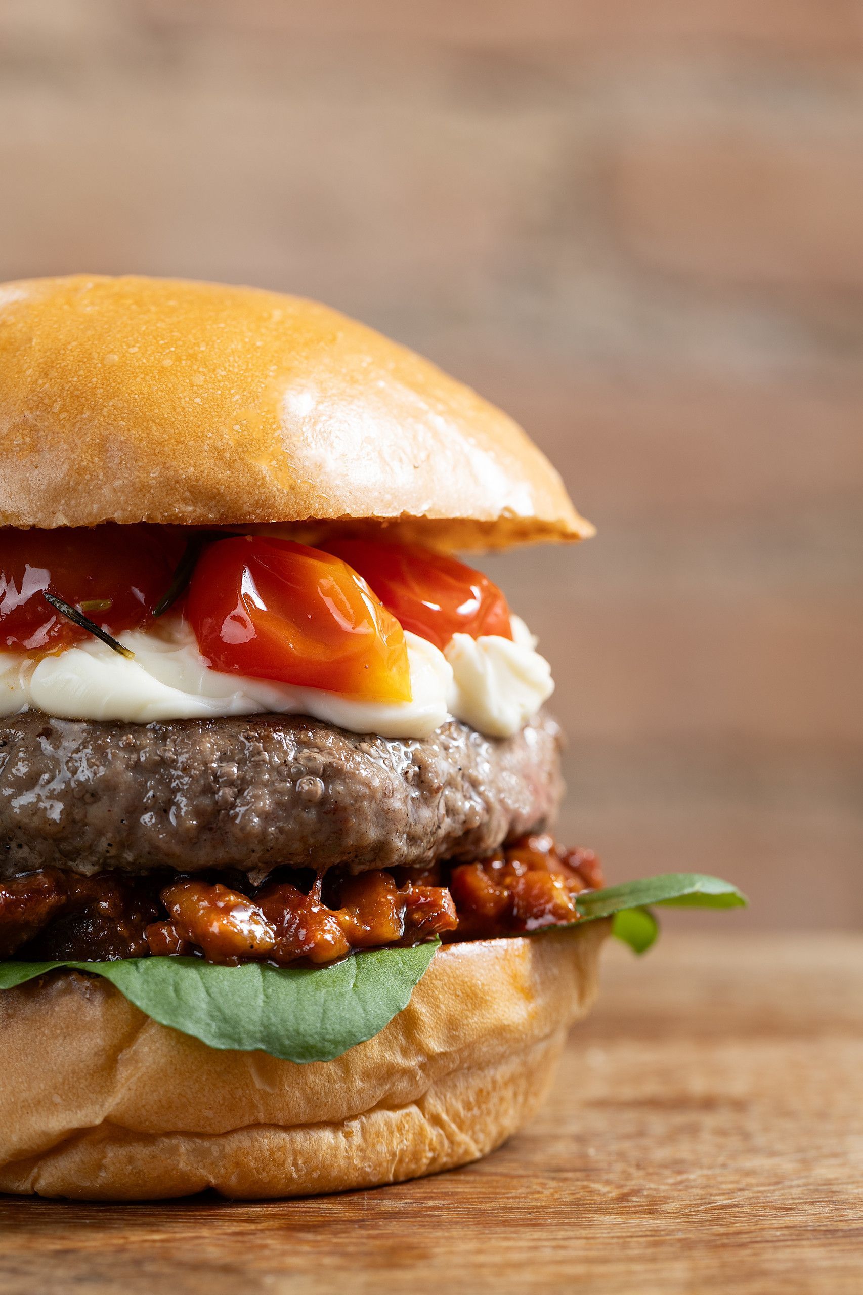Close-up de um cheeseburger suculento com tomate, queijo, alface e molho sobre uma superfície de madeira.