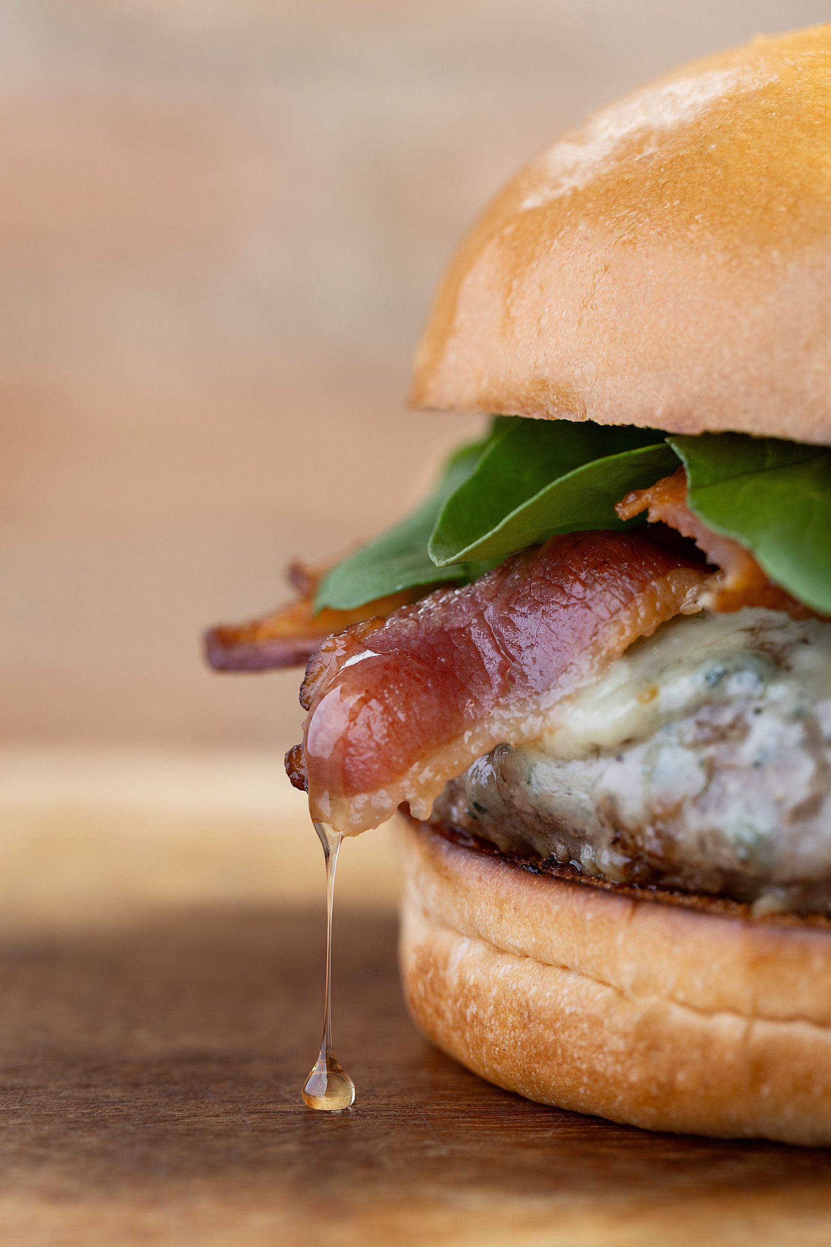Close-up de um cheeseburger com bacon, queijo derretido, alface e molho escorrendo em um pão.