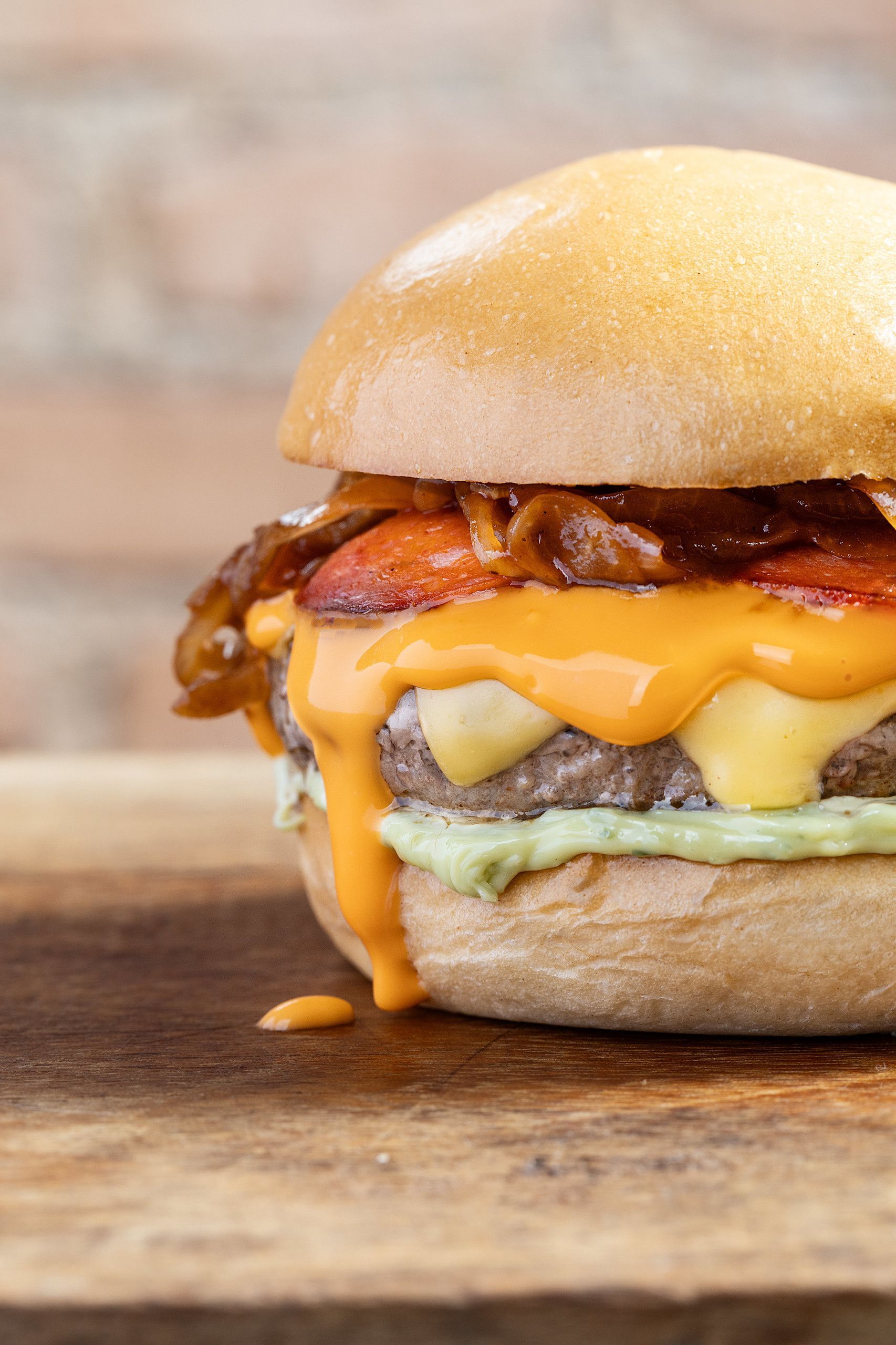 Close-up de um cheeseburger com queijo derretido e bacon em uma tábua de madeira.