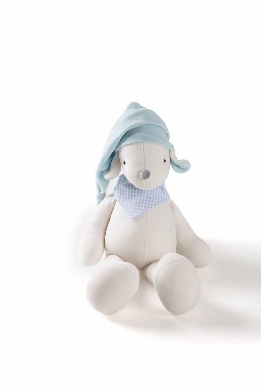 Boneca de pelúcia com chapéu e cachecol azuis, sentada sobre um fundo branco.
