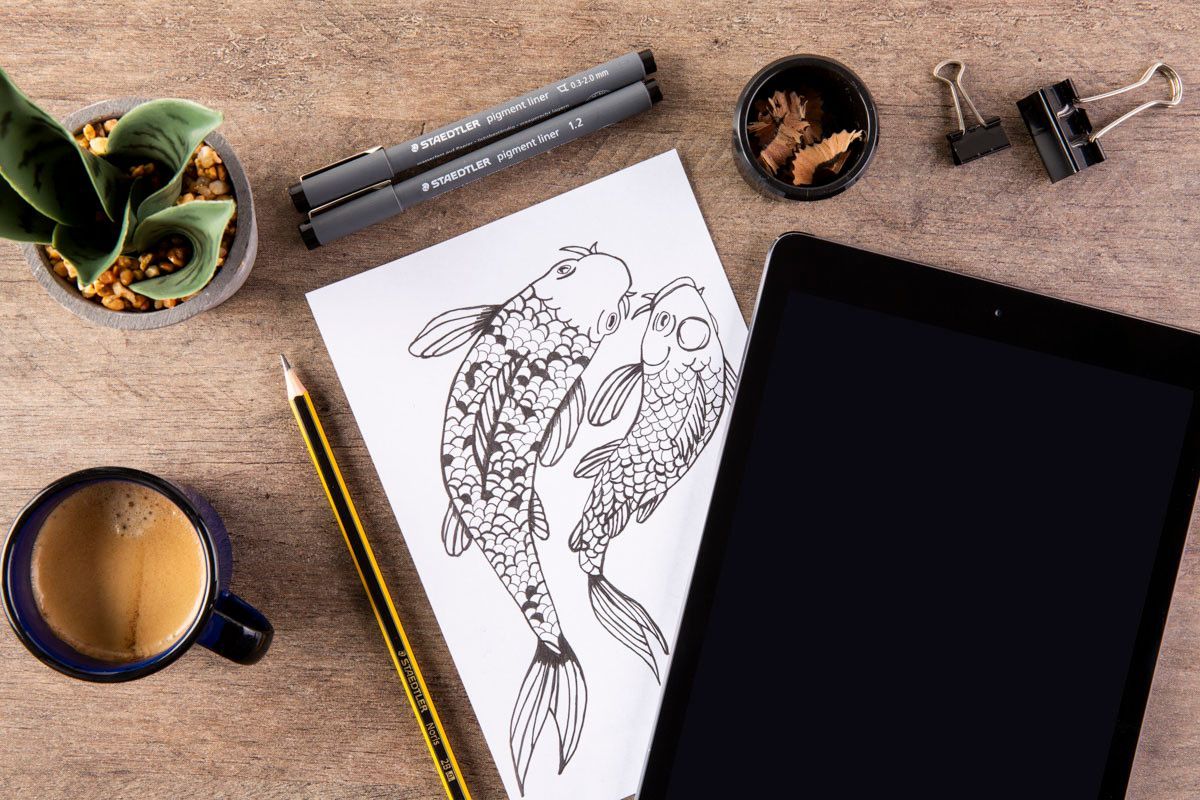 Esboço de um inseto em papel ao lado de um tablet, lápis, xícara de café e materiais de desenho sobre uma mesa de madeira.