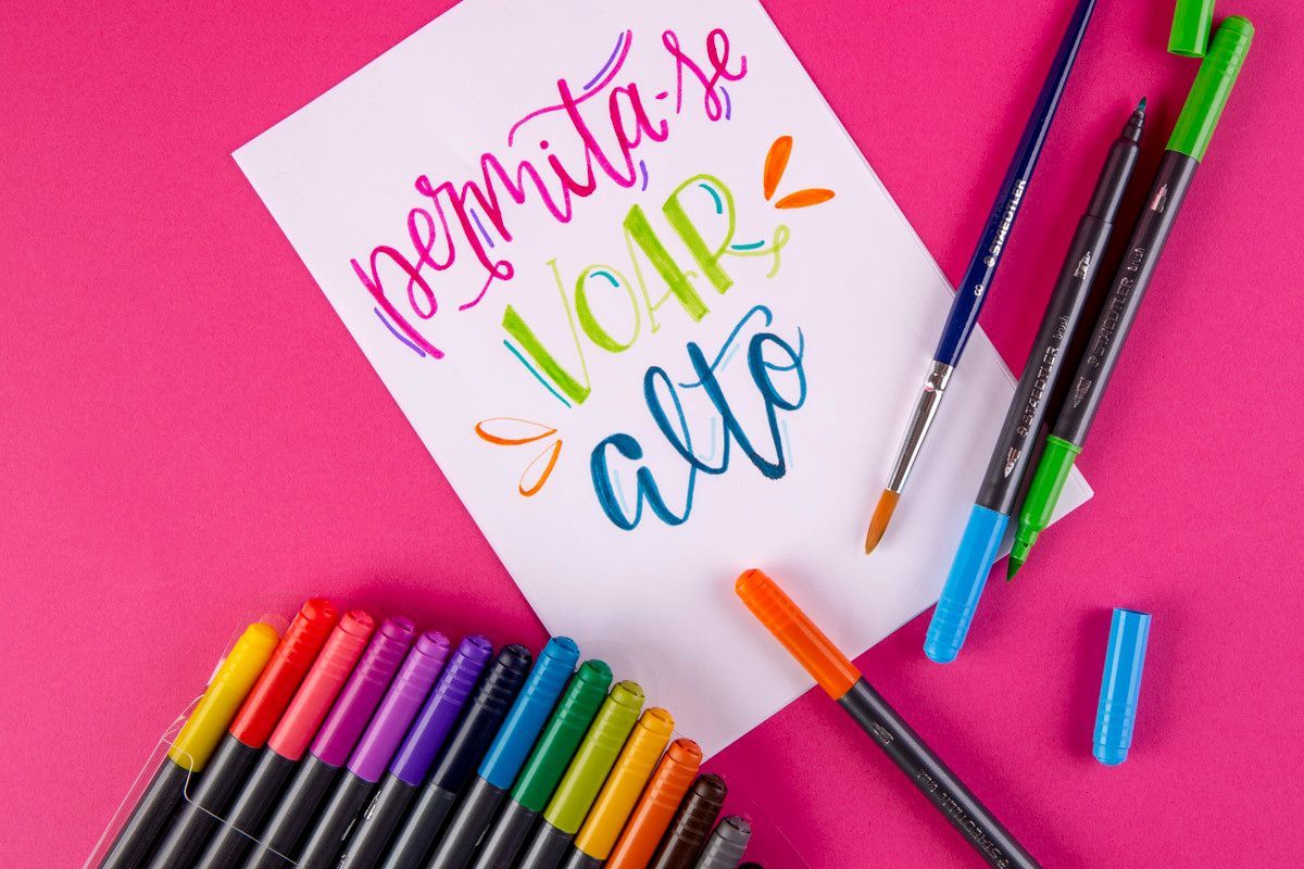 Papelaria colorida em volta de um bilhete com a frase “personalize sua vida” sobre um fundo rosa vibrante.