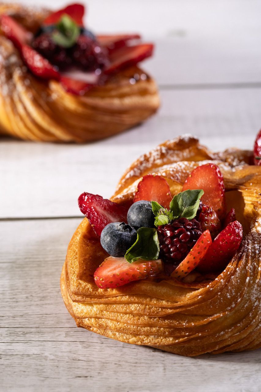 Pastéis com cobertura de frutas e polvilhados com açúcar de confeiteiro sobre uma mesa branca.