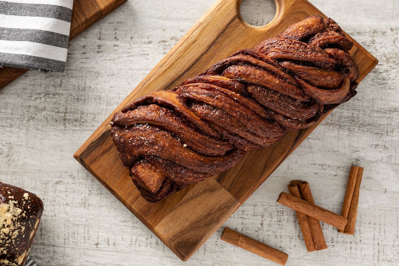 Bolo de chocolate em forma de pão, polvilhado com açúcar e canela, sobre uma tábua de madeira rústica.