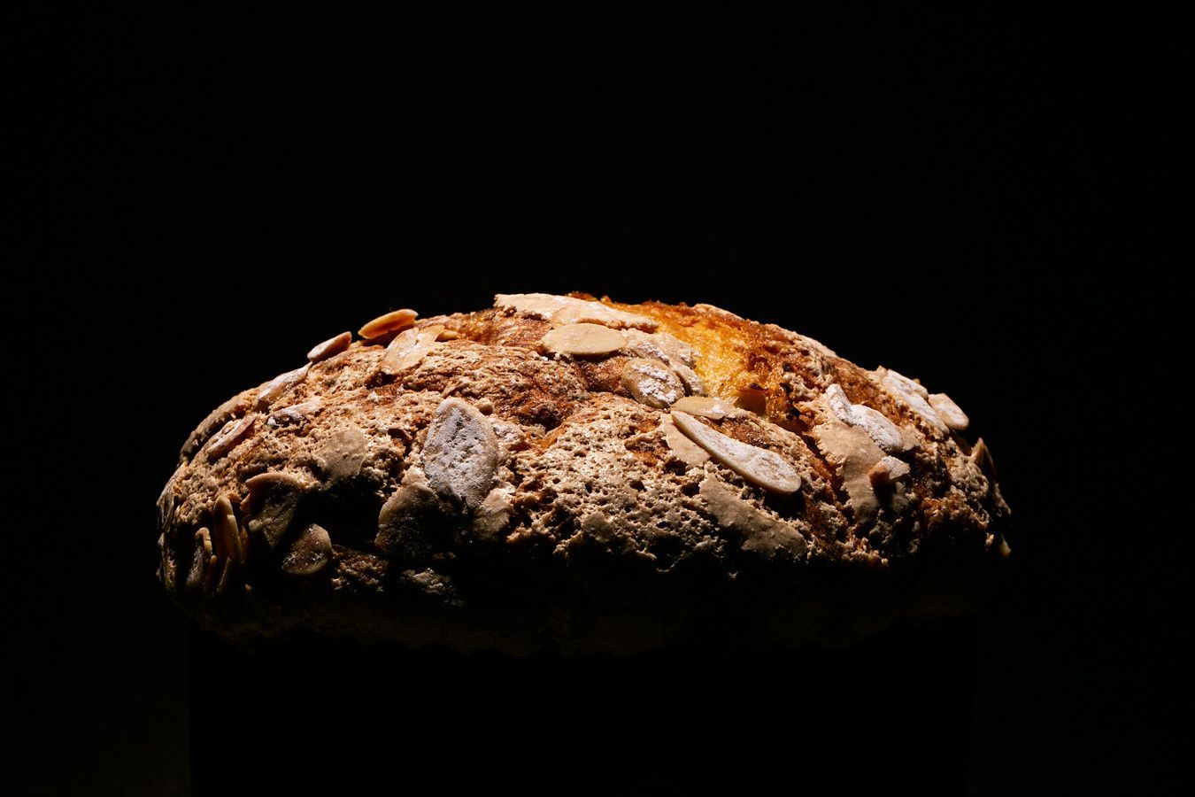 Um pão rústico com a casca rachada, iluminado contra um fundo preto.