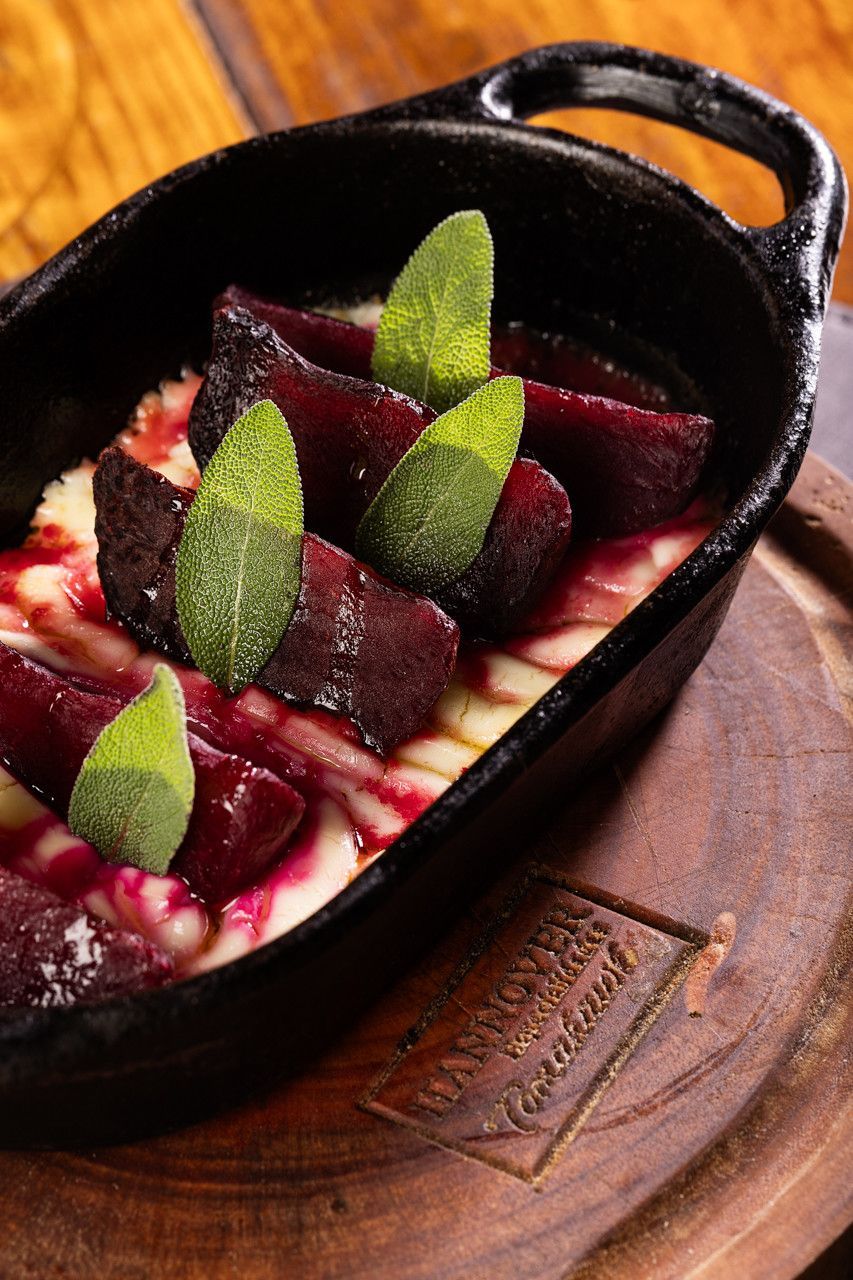 Sobremesa servida em frigideira preta com molho vermelho e folhas de hortelã em tábua de madeira.