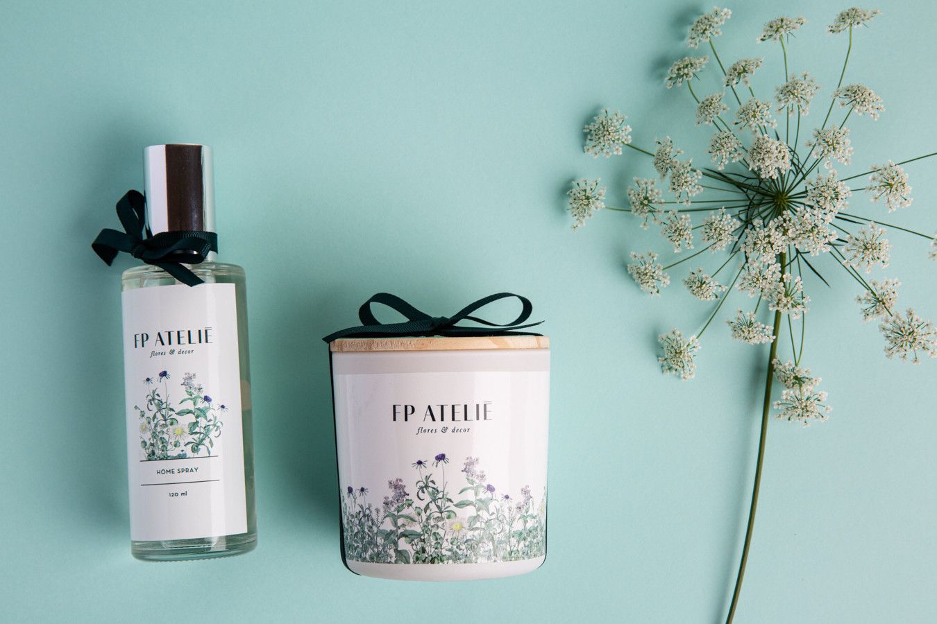 Frasco de perfume, pote de vela e flores secas sobre um fundo azul pastel.