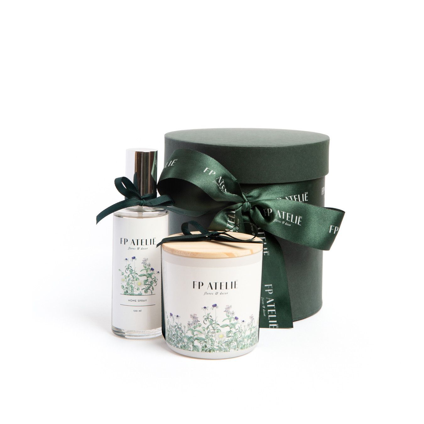 Conjunto para presente com duas velas e uma caixa redonda verde combinando, amarrada com uma fita, sobre um fundo branco.