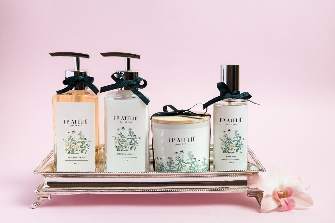 Quatro frascos de perfume com bomba dosadora dispostos em uma bandeja prateada sobre um fundo rosa suave.