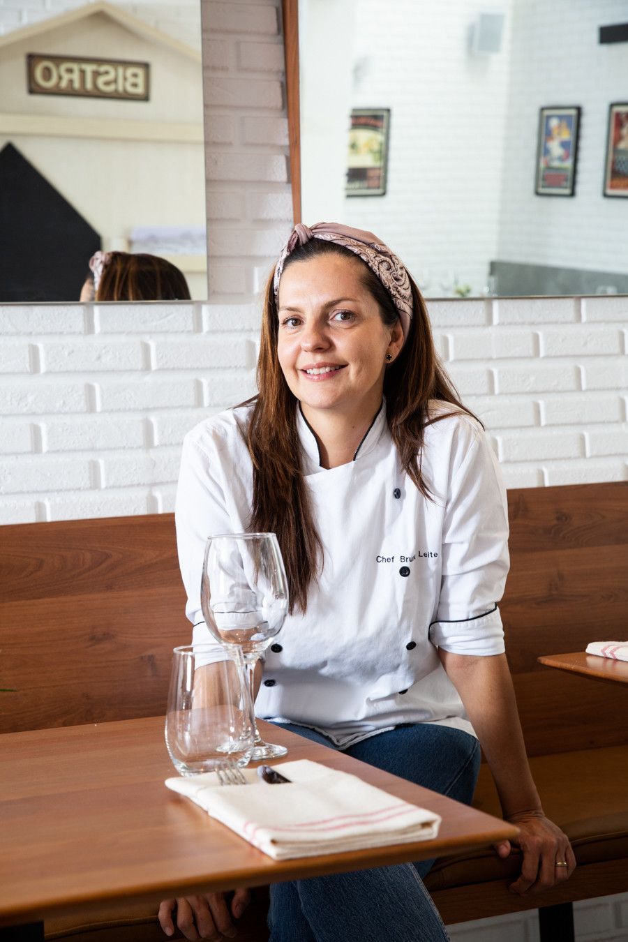 Mulher de avental branco de chef sorrindo em uma mesa de café com uma jarra de água de vidro.