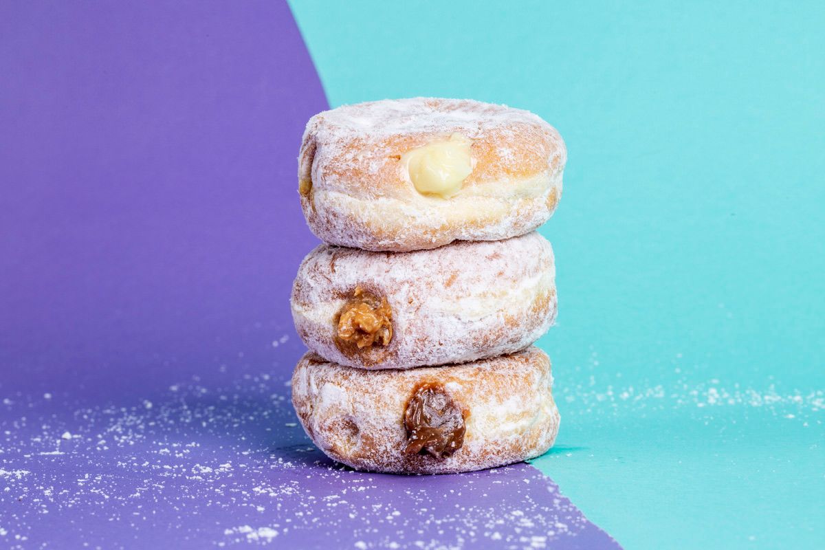 Três donuts açucarados empilhados sobre um fundo roxo e azul-petróleo.