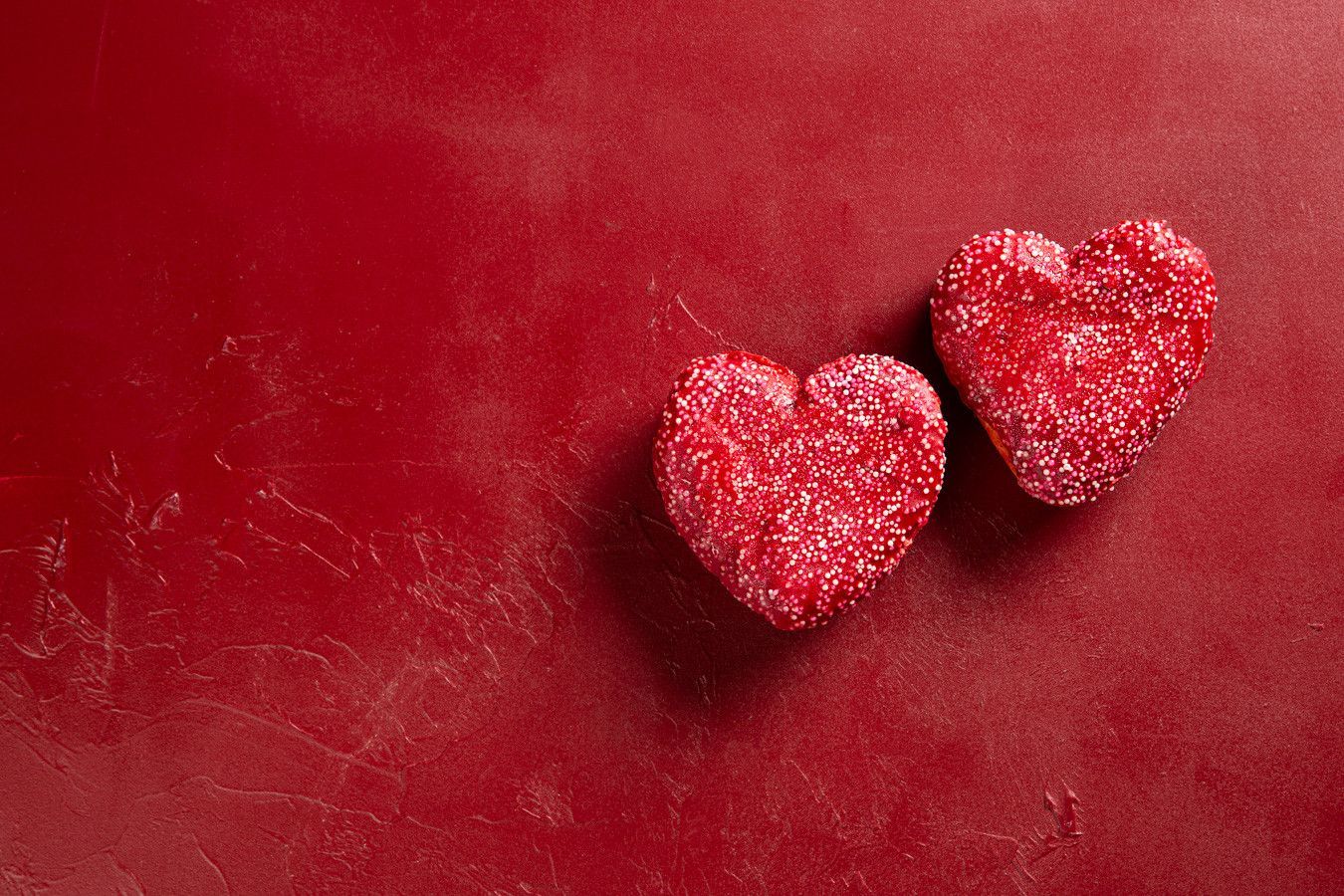 Duas decorações de coração vermelhas com glitter sobre um fundo vermelho texturizado.