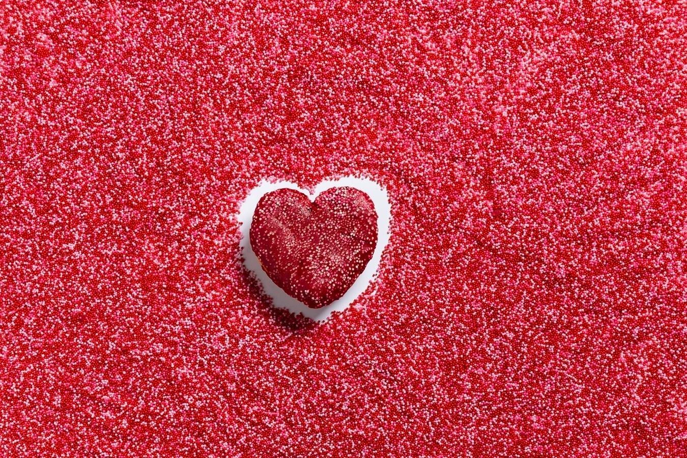 Enfeite vermelho em forma de coração sobre um fundo vermelho brilhante.