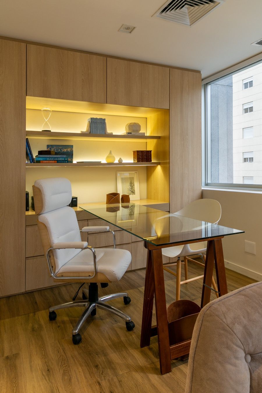 Escritório moderno em casa com estantes de madeira embutidas, mesa de vidro, cadeira de escritório e janela ampla.
