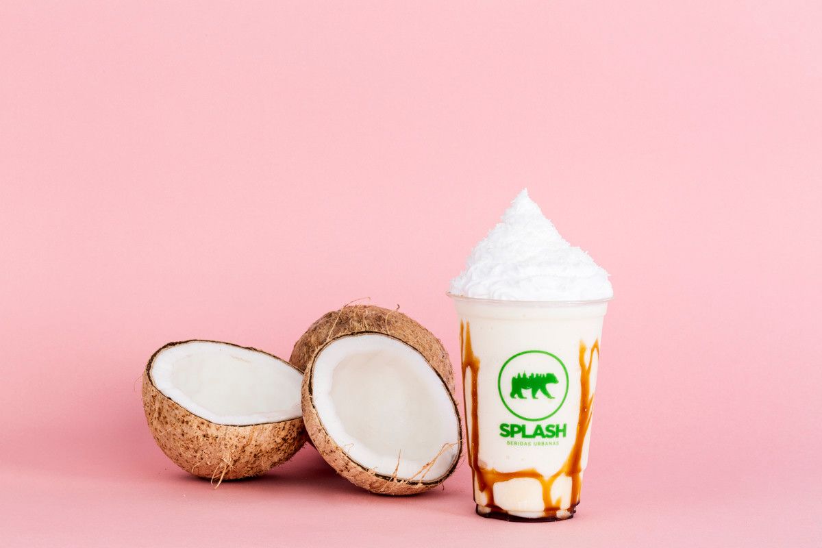Metades de coco ao lado de uma bebida de coco batida em um copo transparente sobre um fundo rosa.