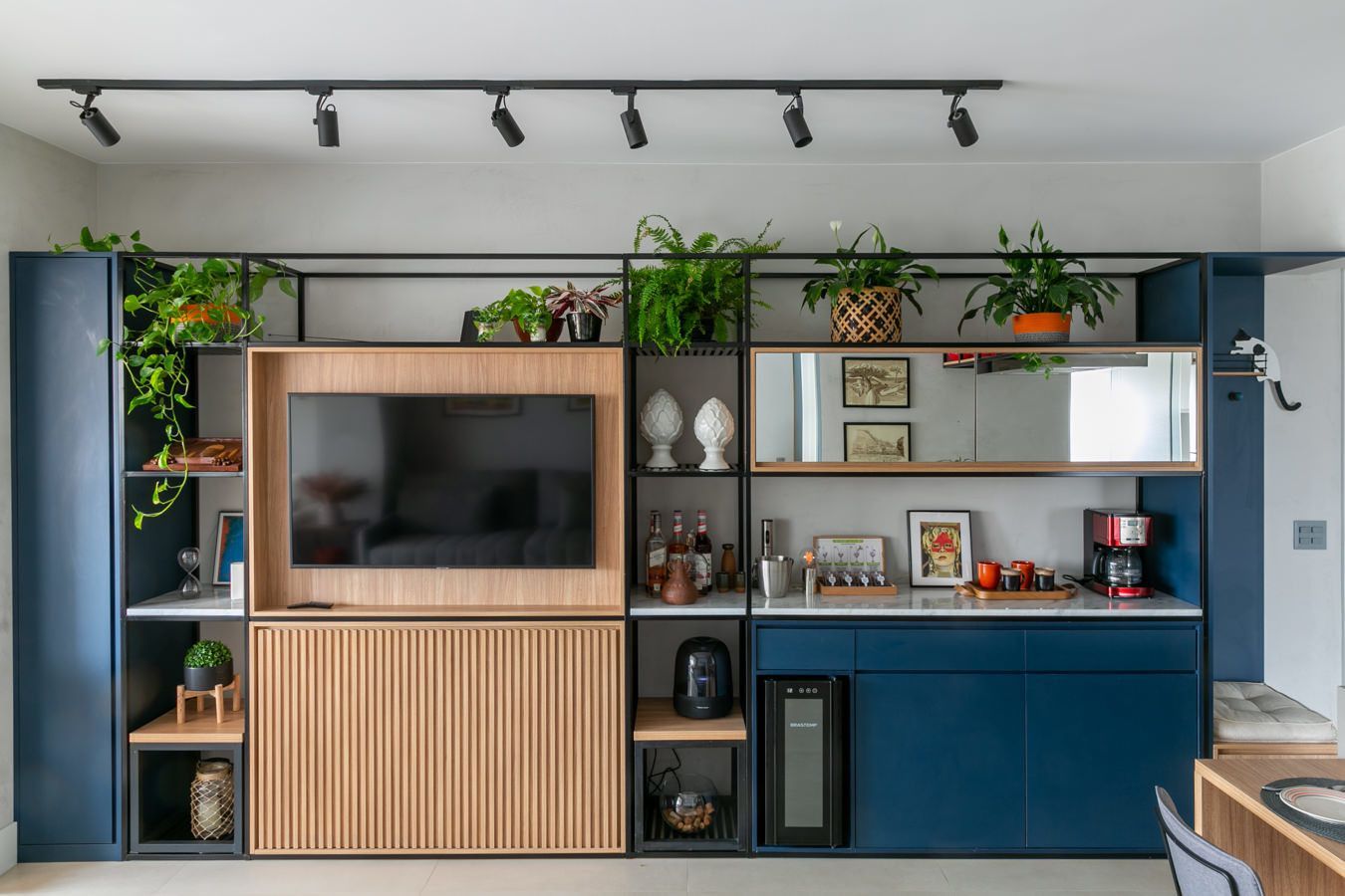 Sala de estar moderna com TV fixada na parede, armários azuis e plantas verdes em prateleiras.