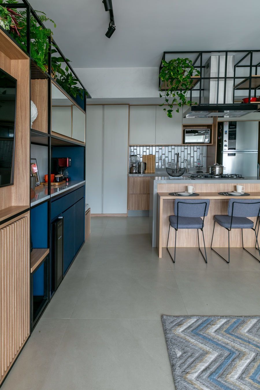 Cozinha e sala de jantar modernas com detalhes em madeira, armários azuis, banquetas e um tapete estampado.