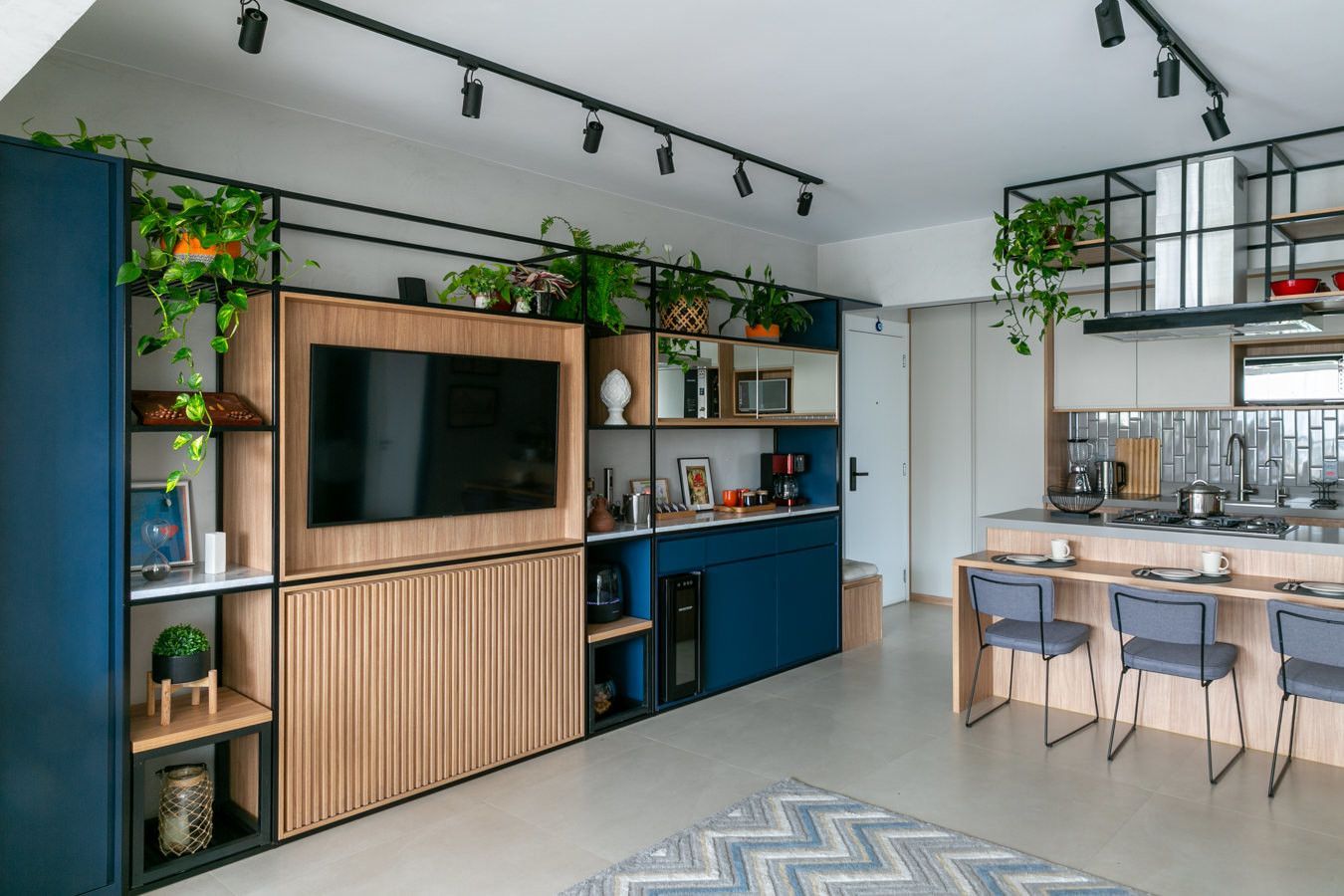 Sala de estar moderna em conceito aberto com parede para TV, armários azuis, plantas de interior e mesa de jantar com cadeiras.