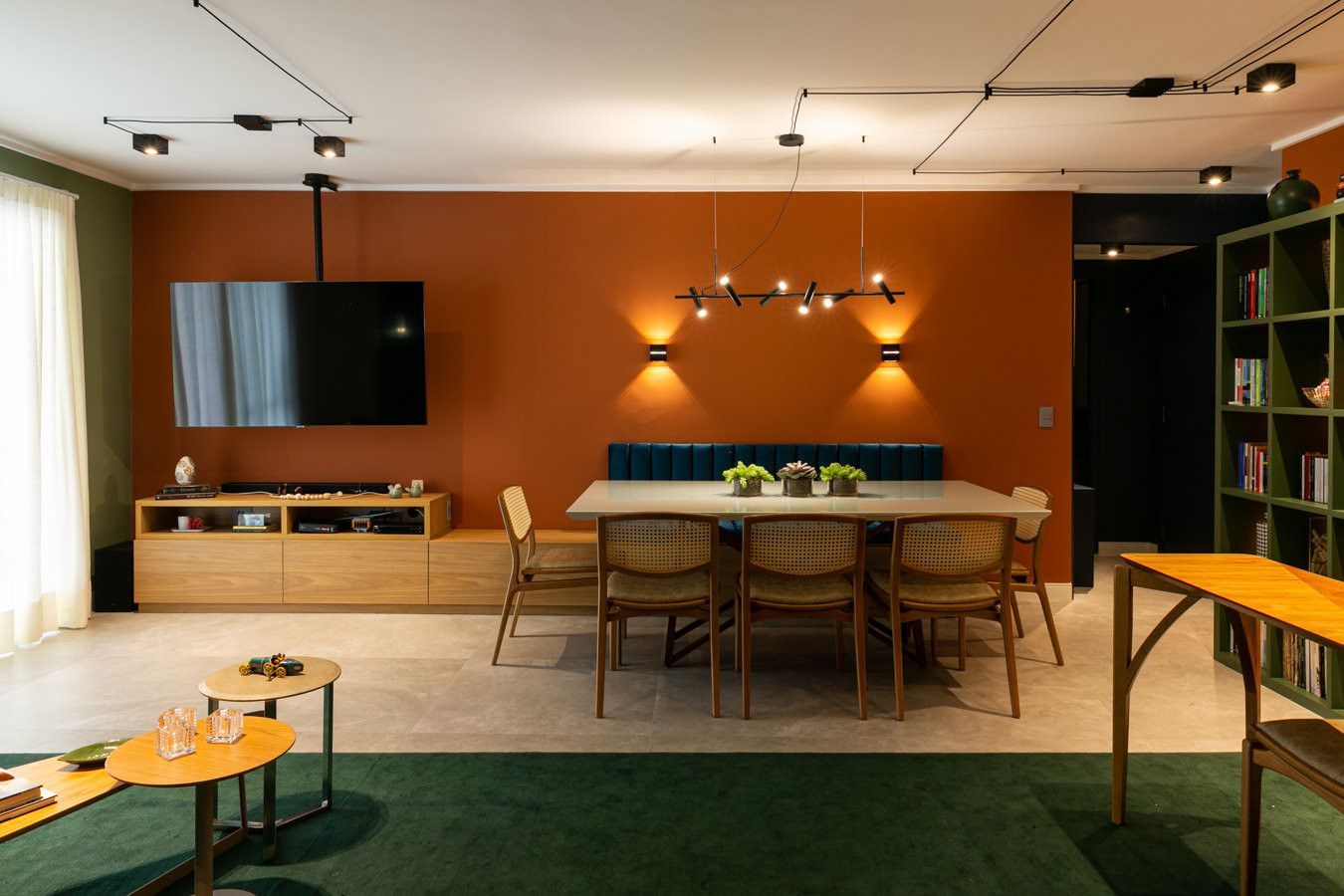 Sala de estar moderna com parede de destaque em laranja, TV, mesa de jantar, prateleiras e tapete verde.