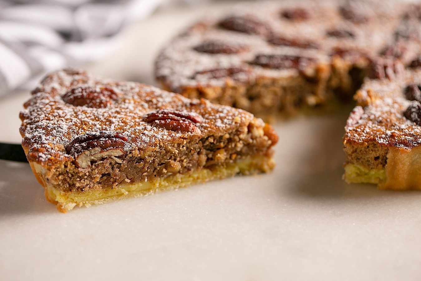 Fatias de torta polvilhadas com açúcar de confeiteiro e recheadas com massa escura, servidas em um prato branco.