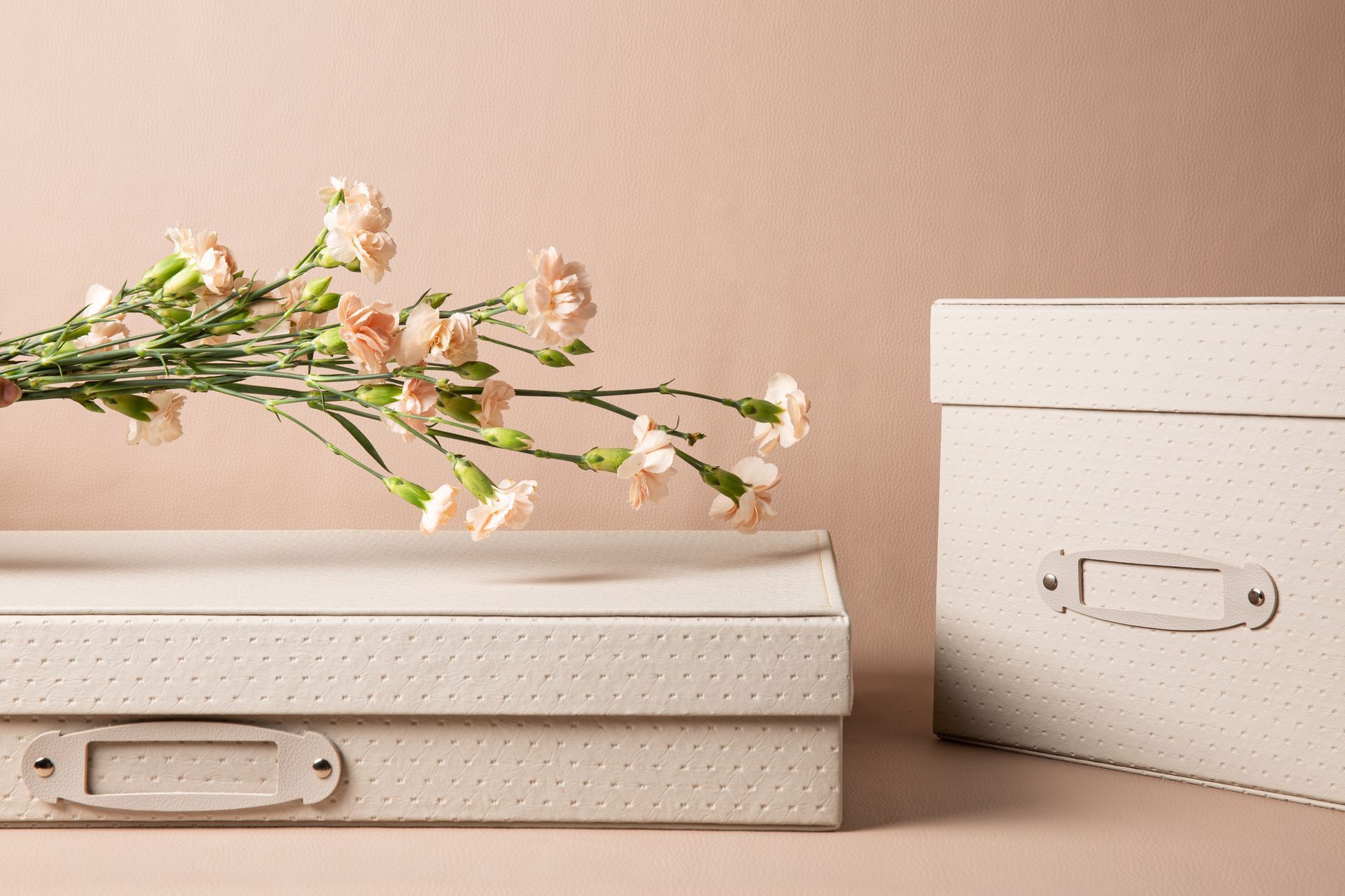 Caixas organizadoras em tons pastel com uma delicada flor rosa sobre fundo bege.