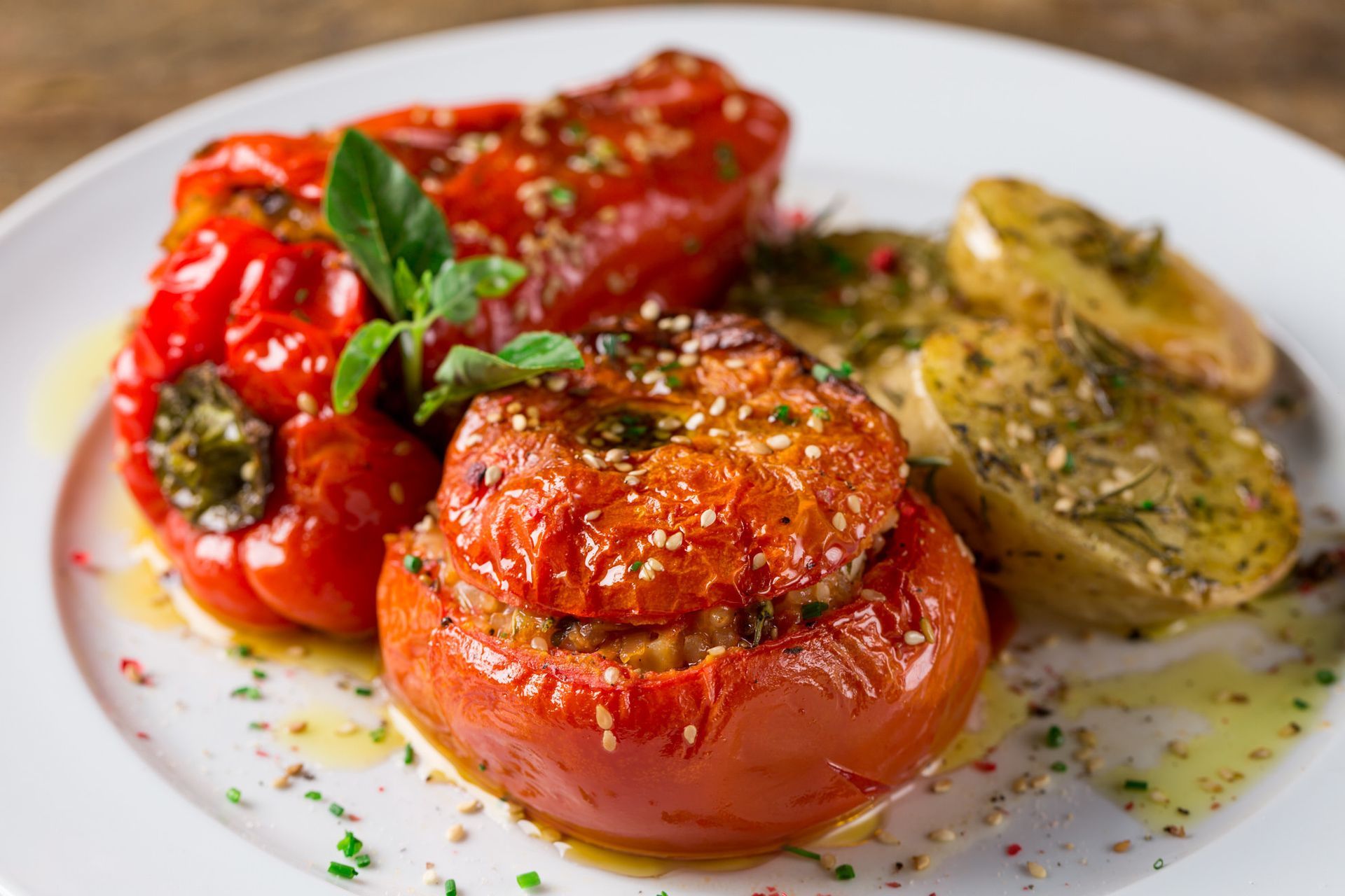 Tomates e pimentões recheados e assados, decorados com manjericão e ervas, servidos em um prato branco.